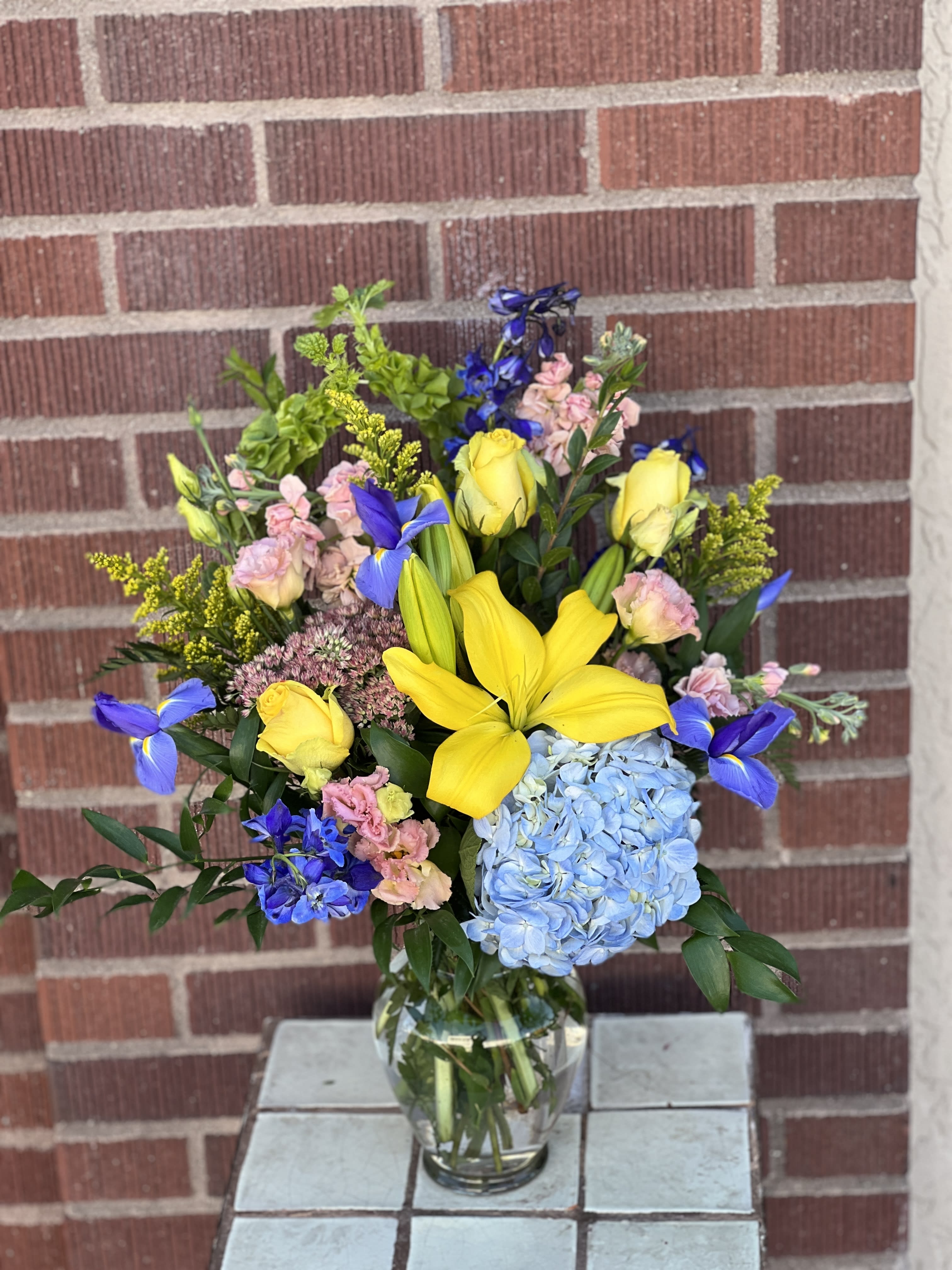 Mixed bouquet with yellow lilies, blue hydrangea, and pink flowers in a glass vase