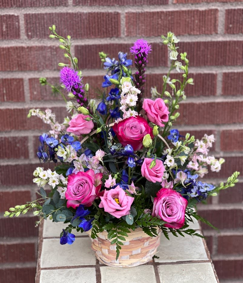 Mixed pink and blue flower arrangement in a woven basket