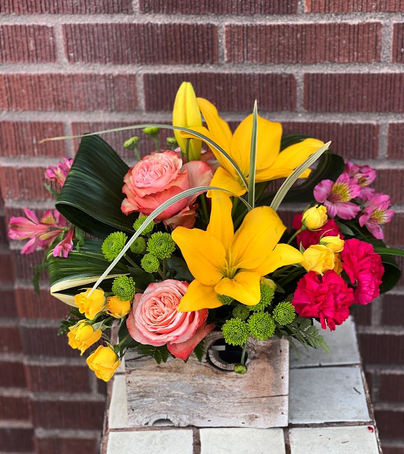 Colorful bouquet with yellow lilies, pink roses, and bright pink carnations in a wooden box