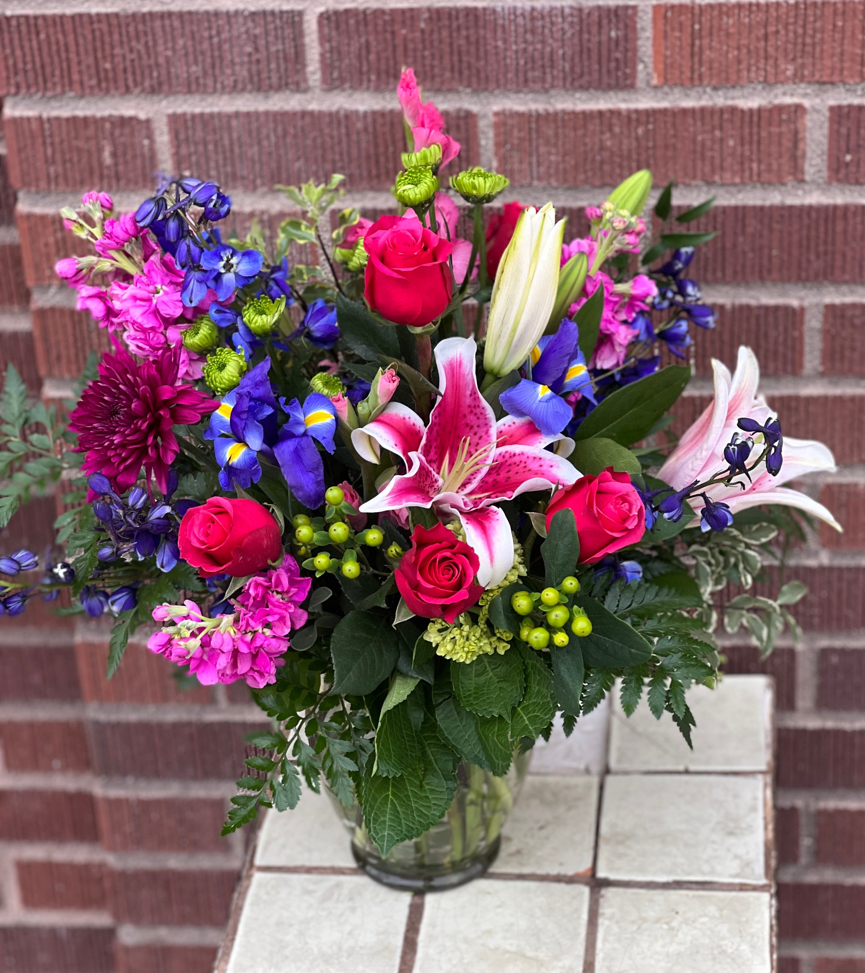 Mixed bouquet of pink roses, lilies, and blue flowers in a glass vase