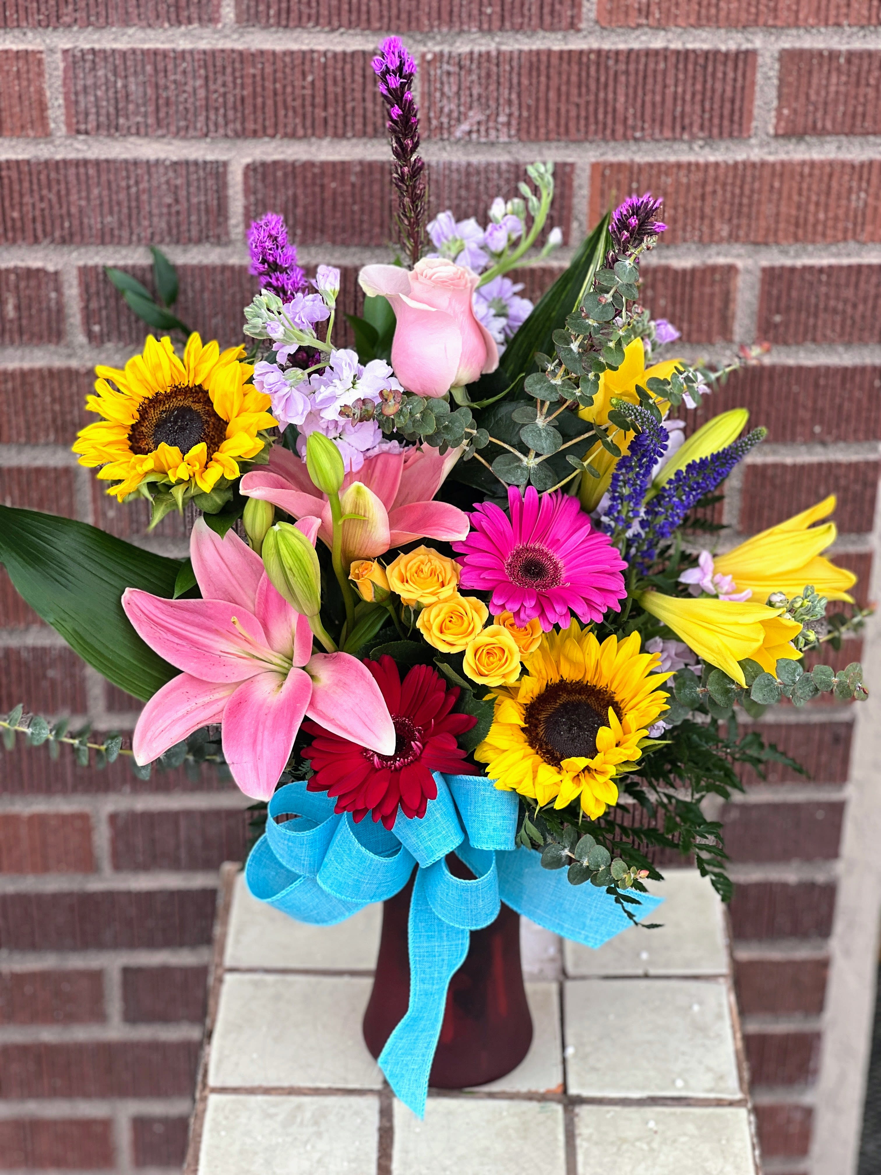 Colorful mixed bouquet with lilies, sunflowers, roses, and gerbera daisies in a vase