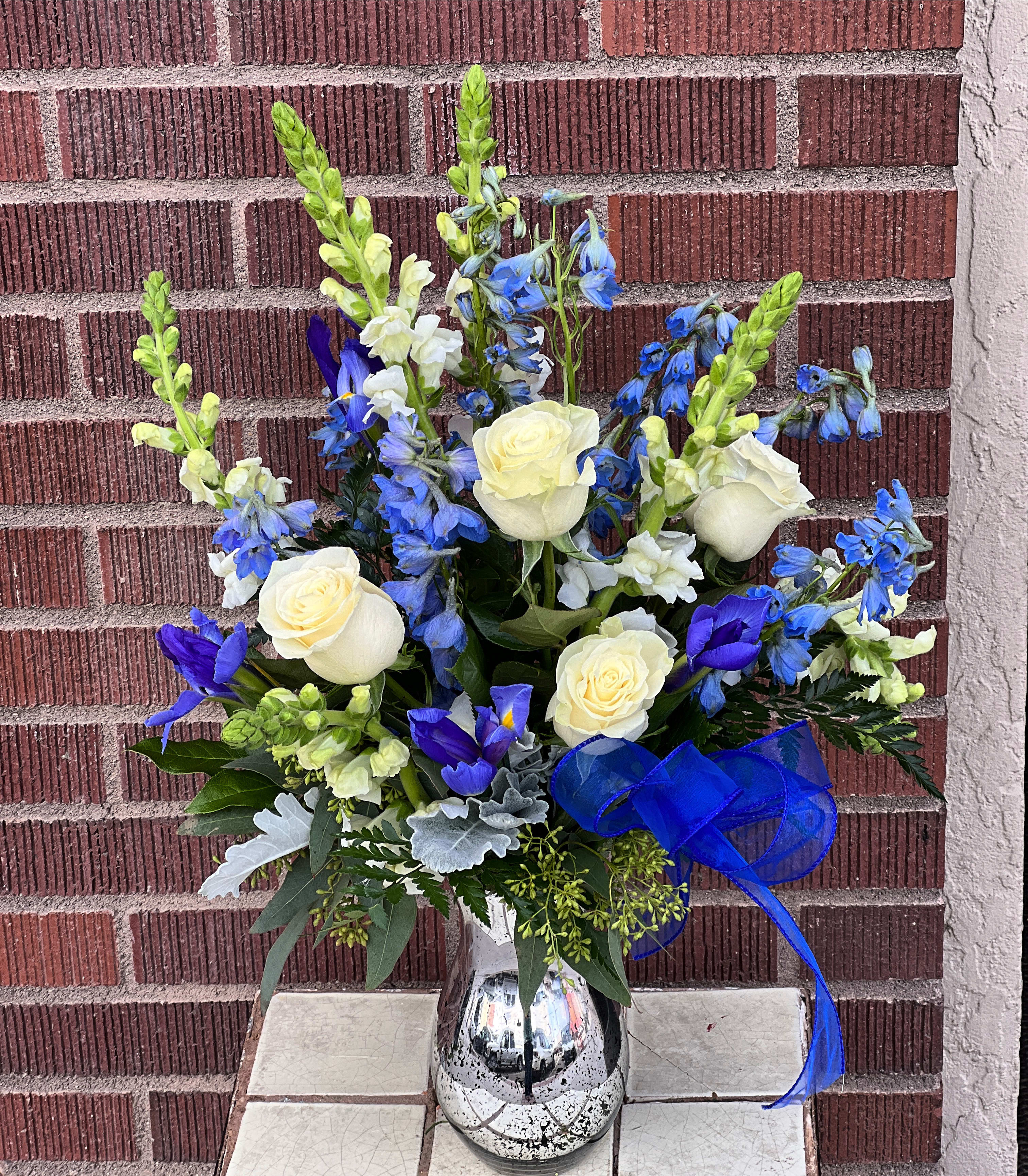 Blue and white floral arrangement in a silver vase with a blue ribbon