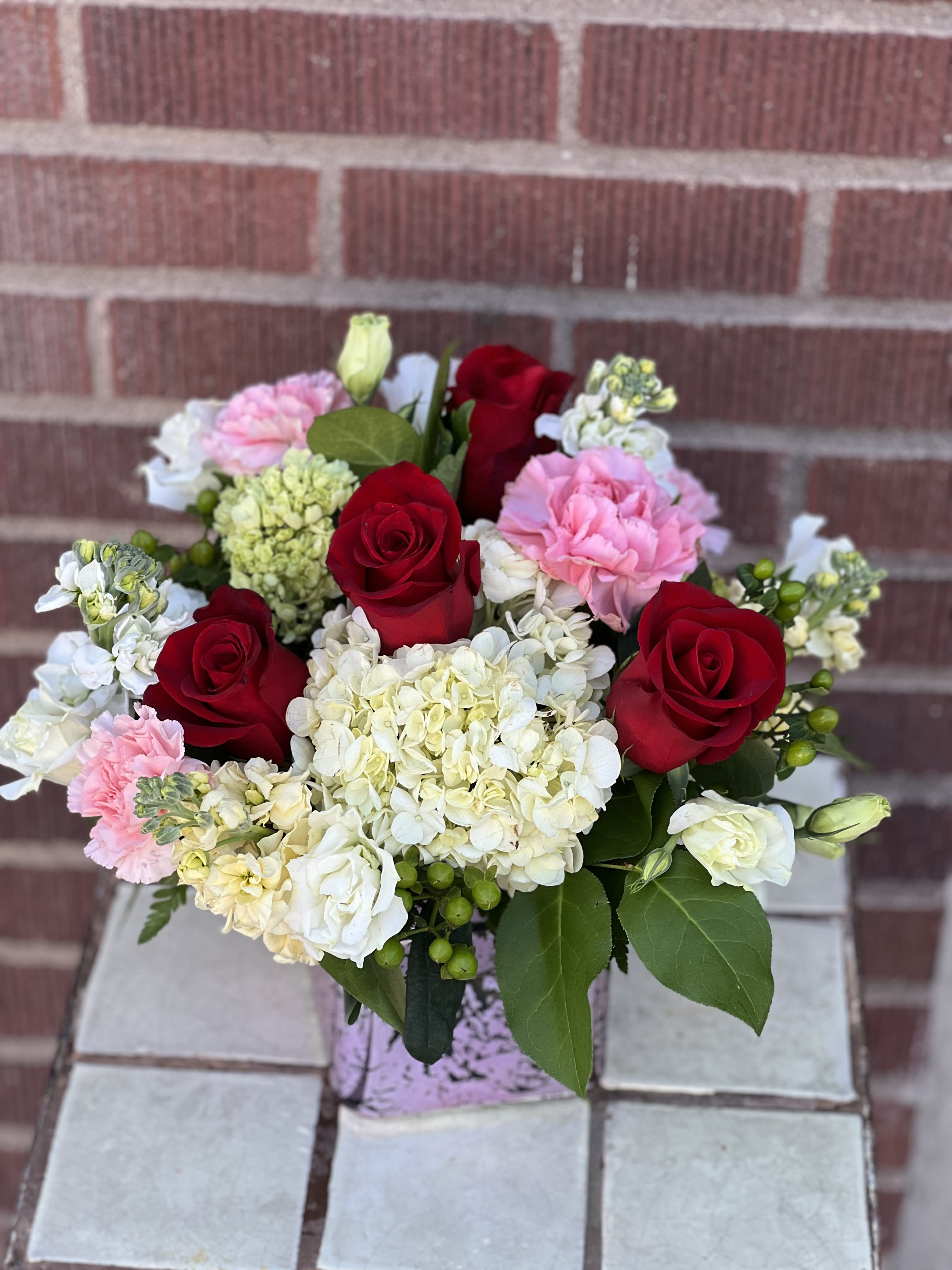 Bouquet of red roses, pink carnations, and white hydrangeas in a vase