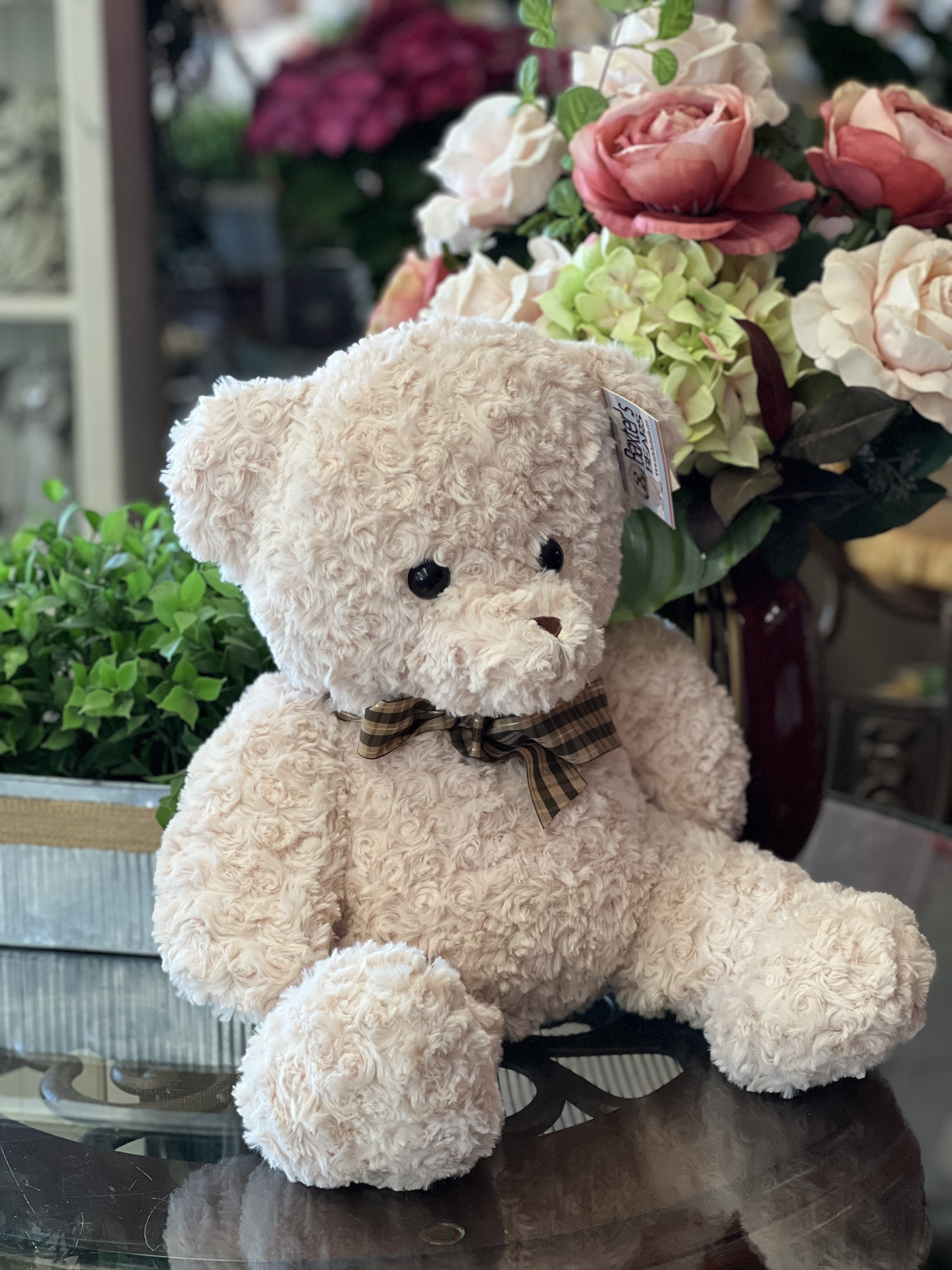 Teddy bear in front of a floral arrangement with pink and cream roses