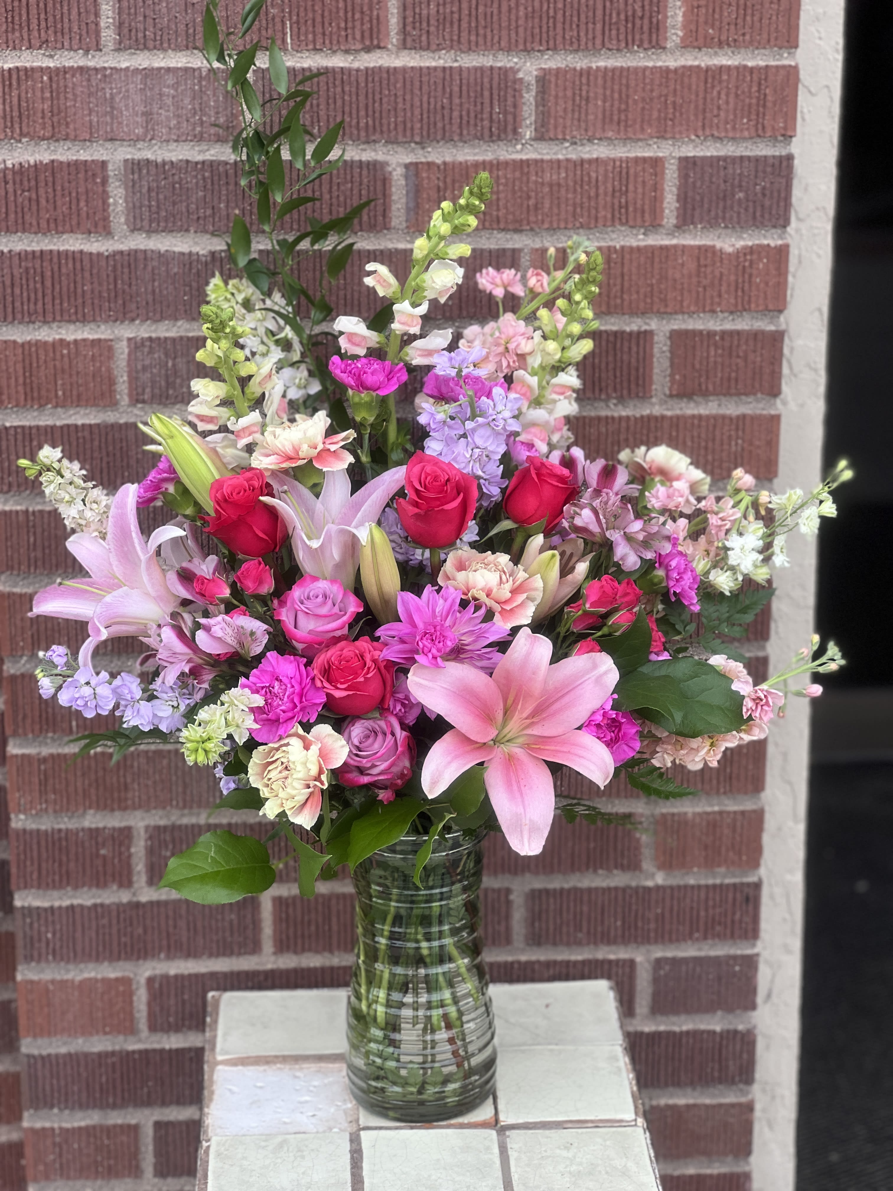 Mixed pink bouquet with roses, lilies, and snapdragons in a glass vase