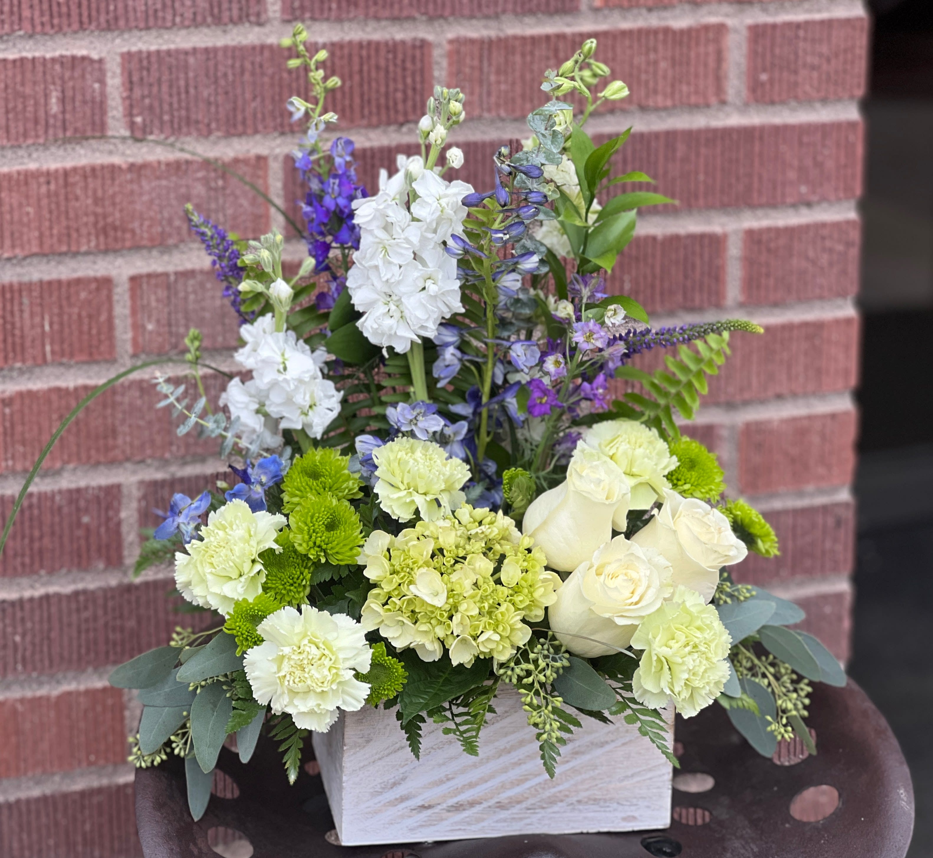 White and green floral arrangement with blue accents in a white container