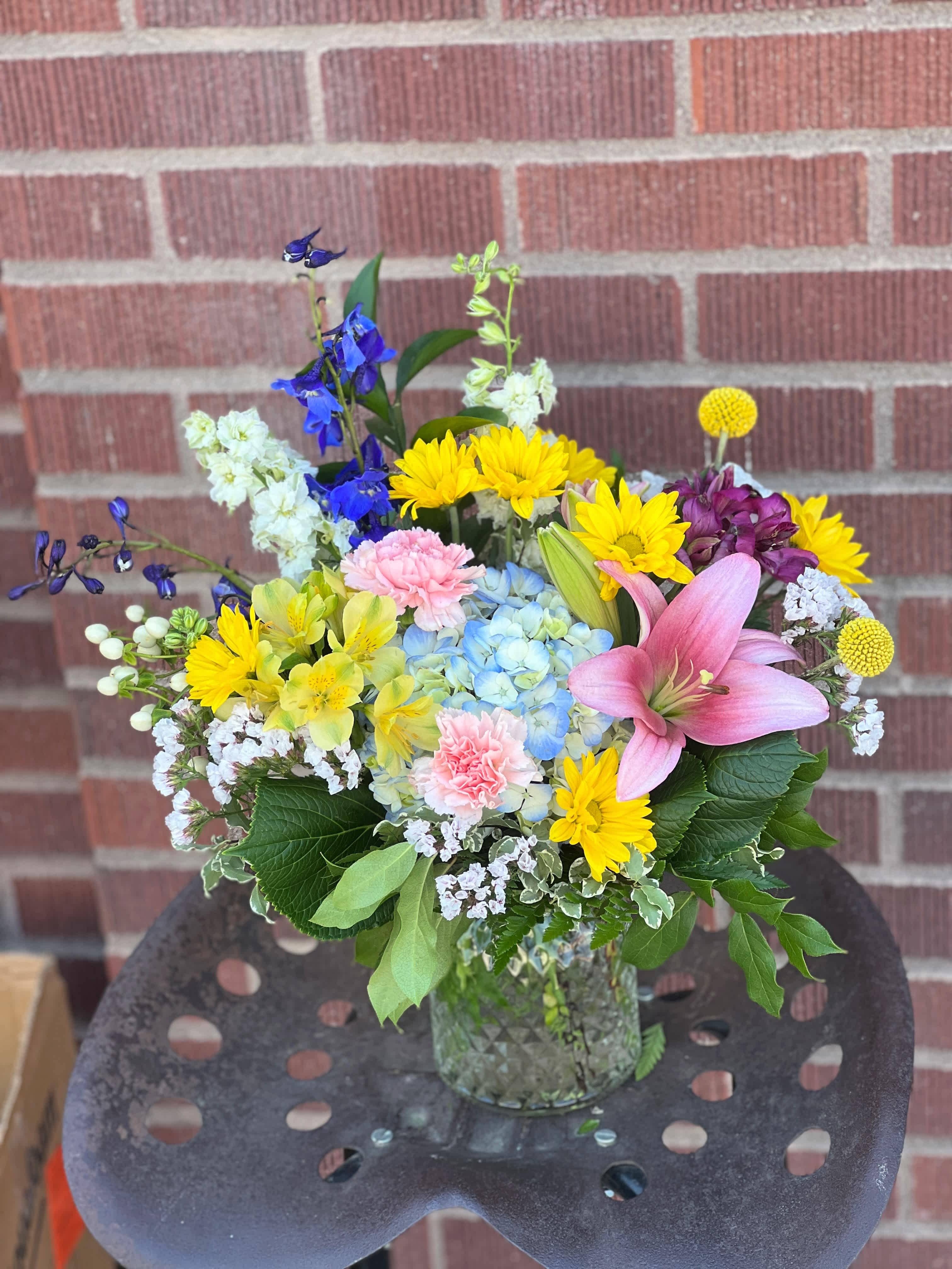 Mixed bouquet in a glass vase with pink lily, blue hydrangea, and yellow daisies