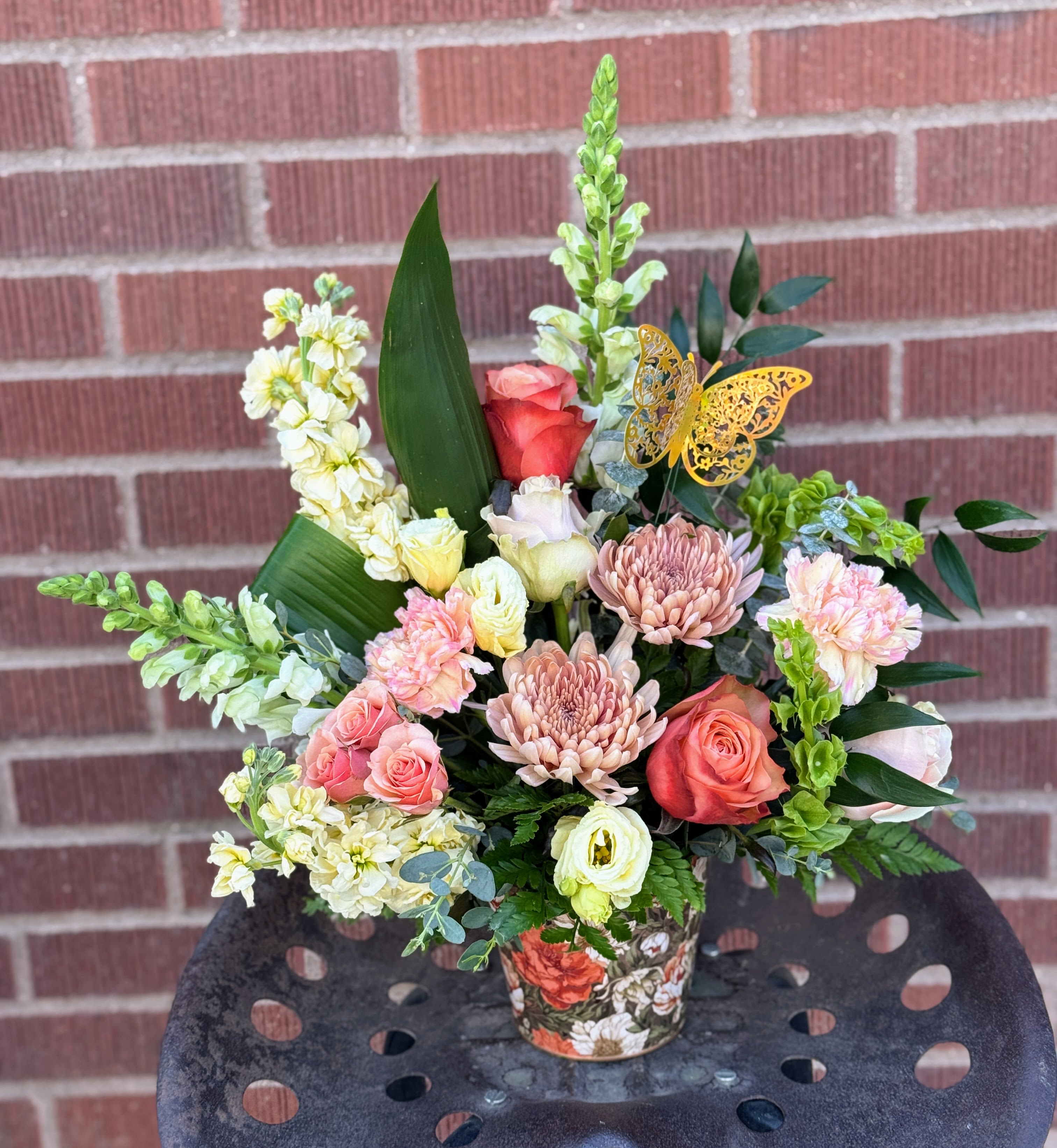 Mixed bouquet in a floral-patterned container with pink and cream flowers