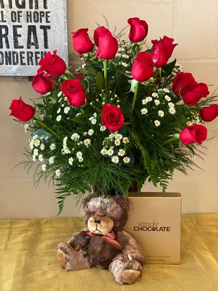 Red roses arranged with small white daisies, a teddy bear, and a chocolate box