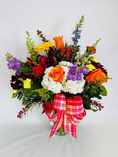 Colorful mixed flower bouquet in a glass vase with a plaid ribbon