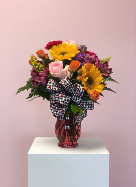 Mixed bouquet of sunflowers, roses, and purple flowers in a red vase