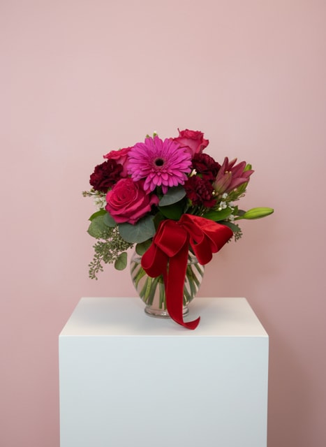 Pink and red flower bouquet in a glass vase with a red ribbon