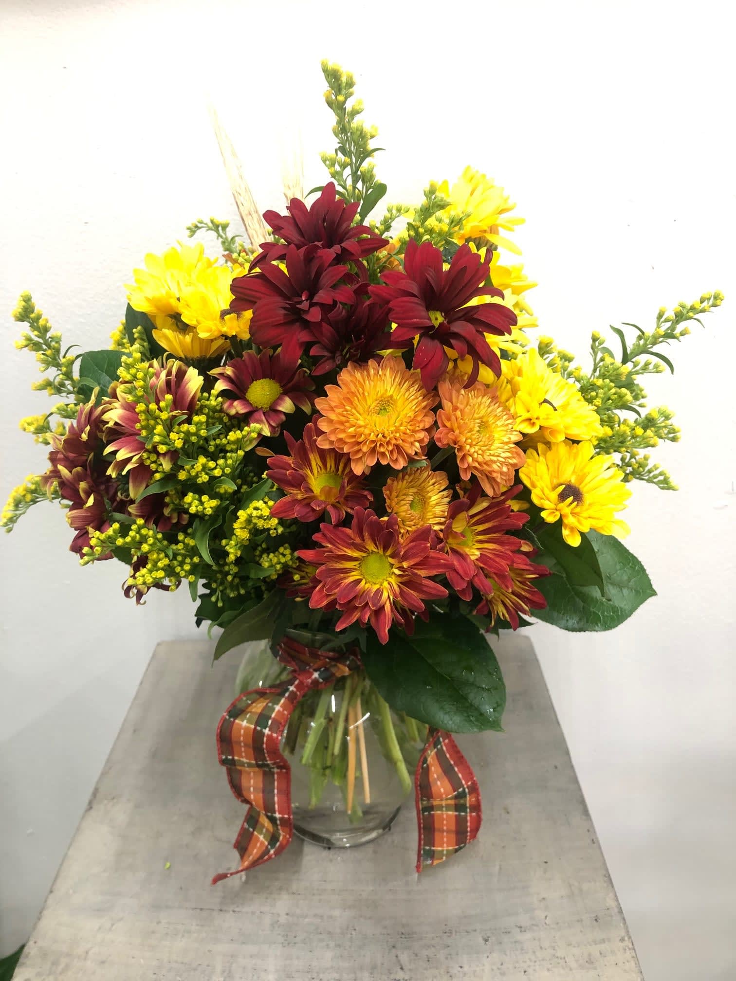 Bouquet of yellow and burgundy chrysanthemums in a glass vase with plaid ribbon