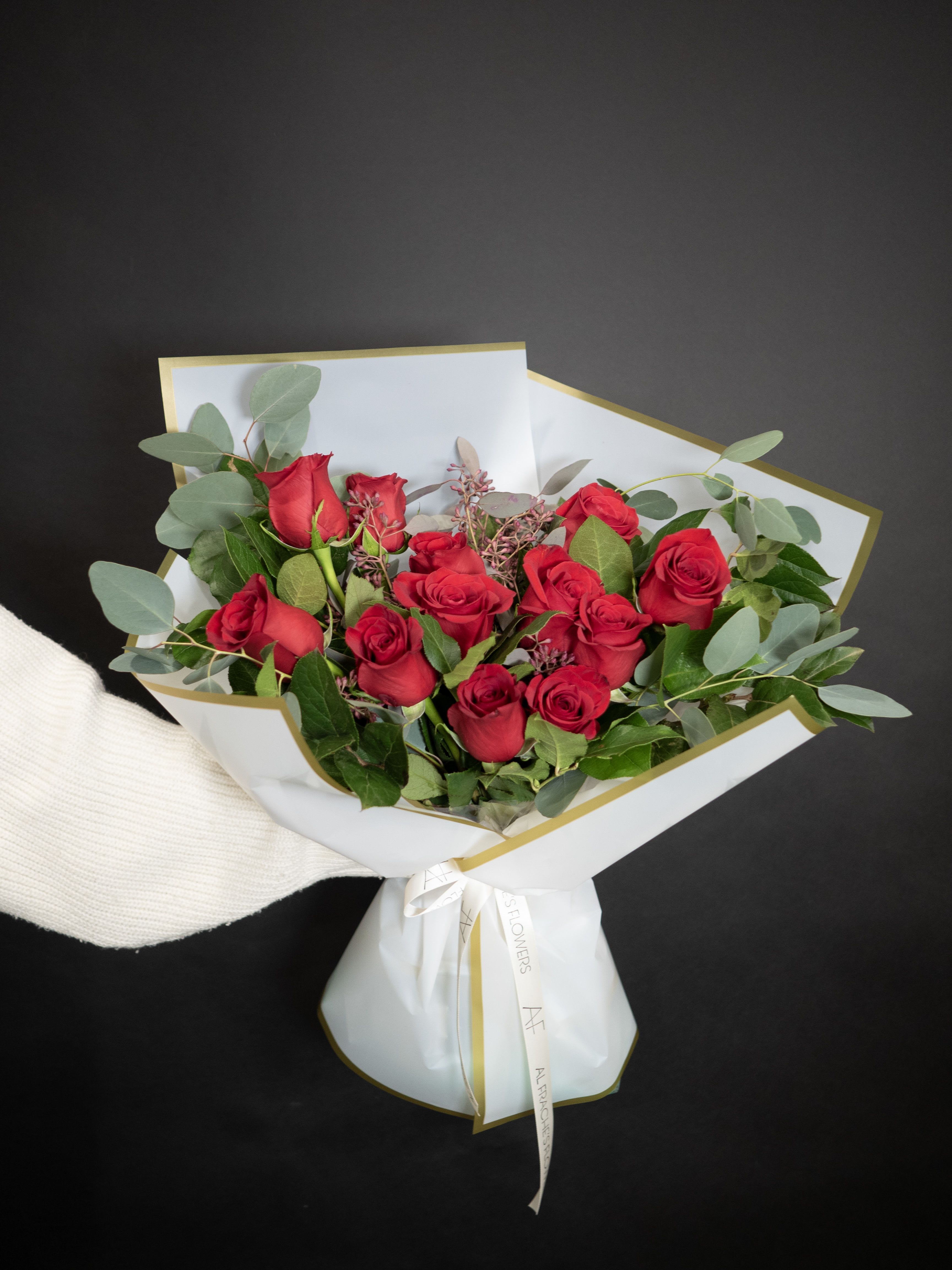 Bouquet of red roses wrapped in white paper with gold trim