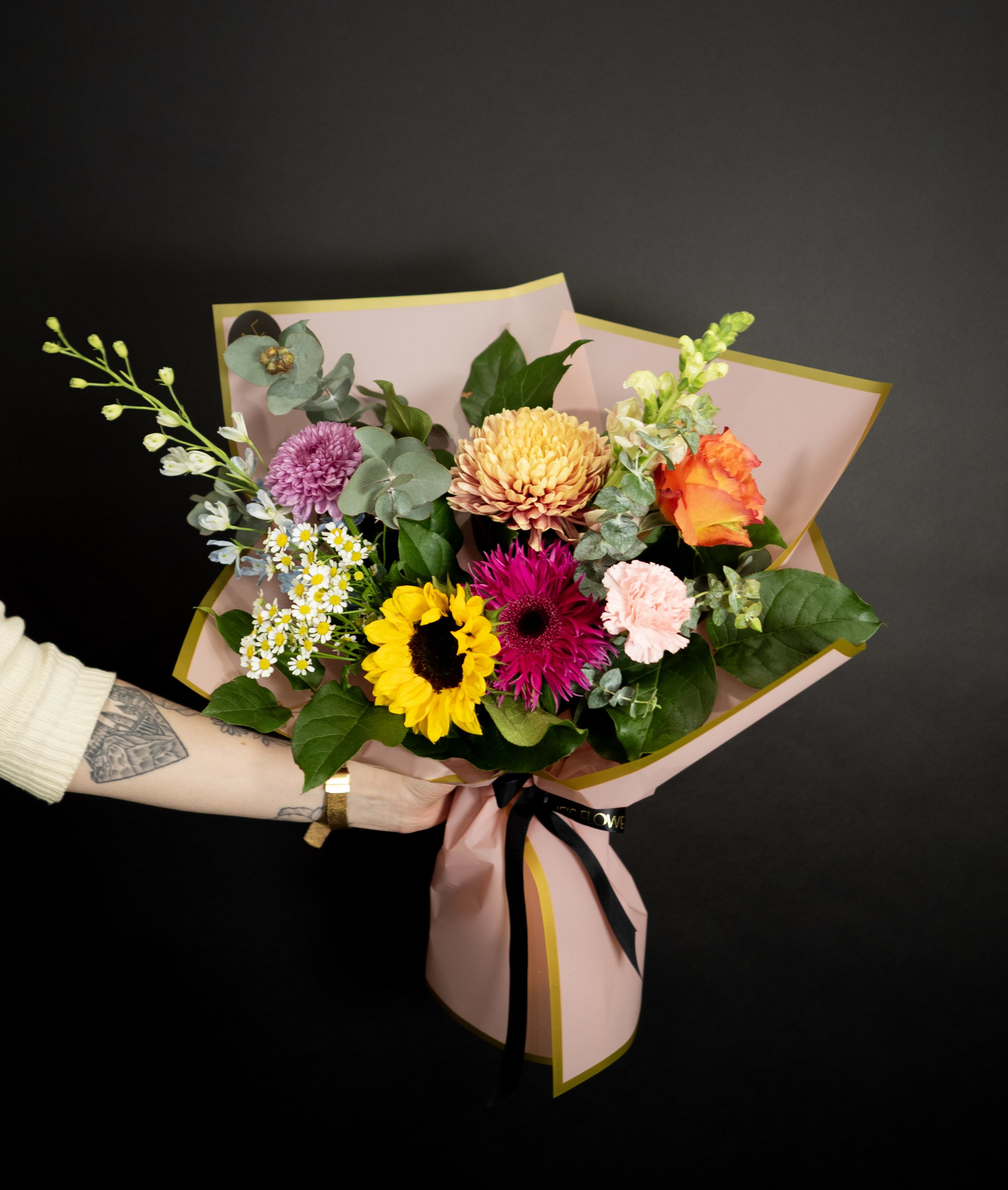 Mixed bouquet with sunflower, roses, and chrysanthemums wrapped in pink paper