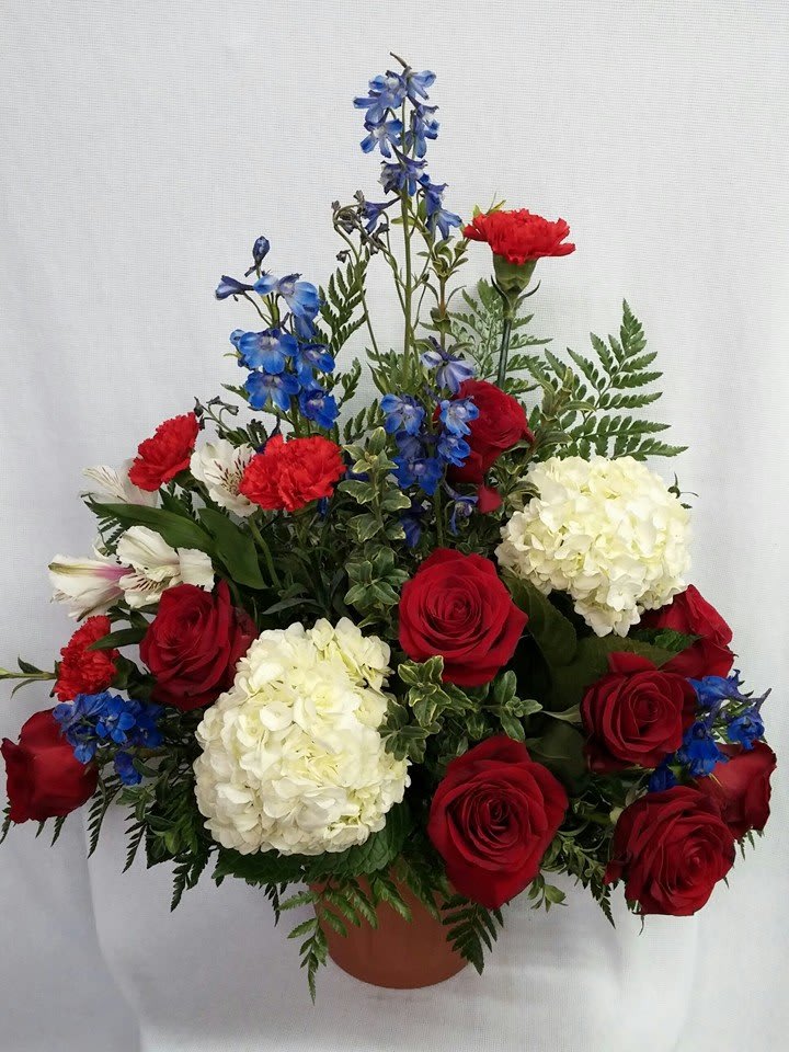 Red roses, white hydrangeas, and blue flowers in a terracotta pot