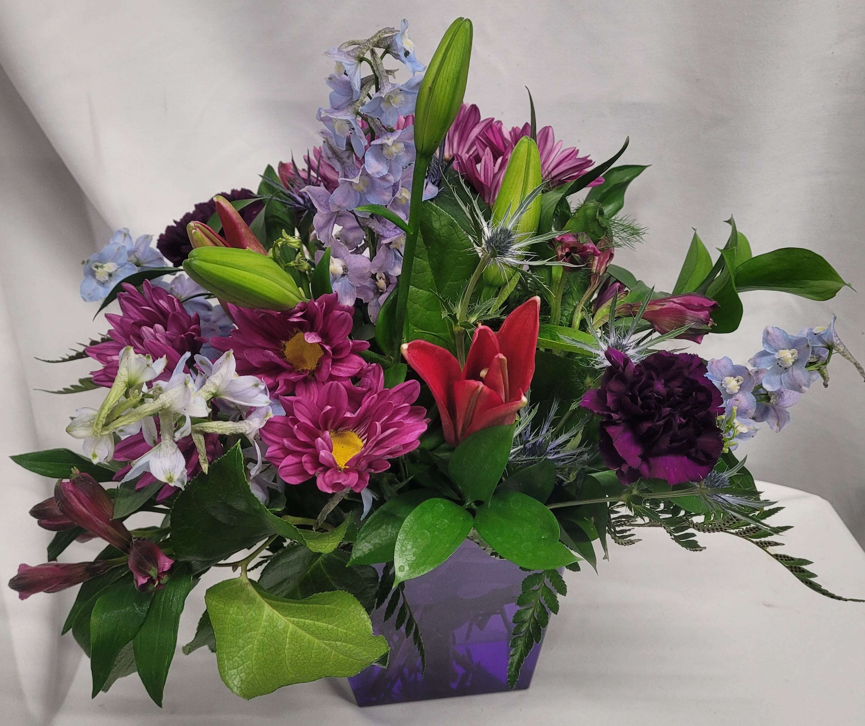 Mixed bouquet with lilies, daisies, and purple flowers in a purple vase