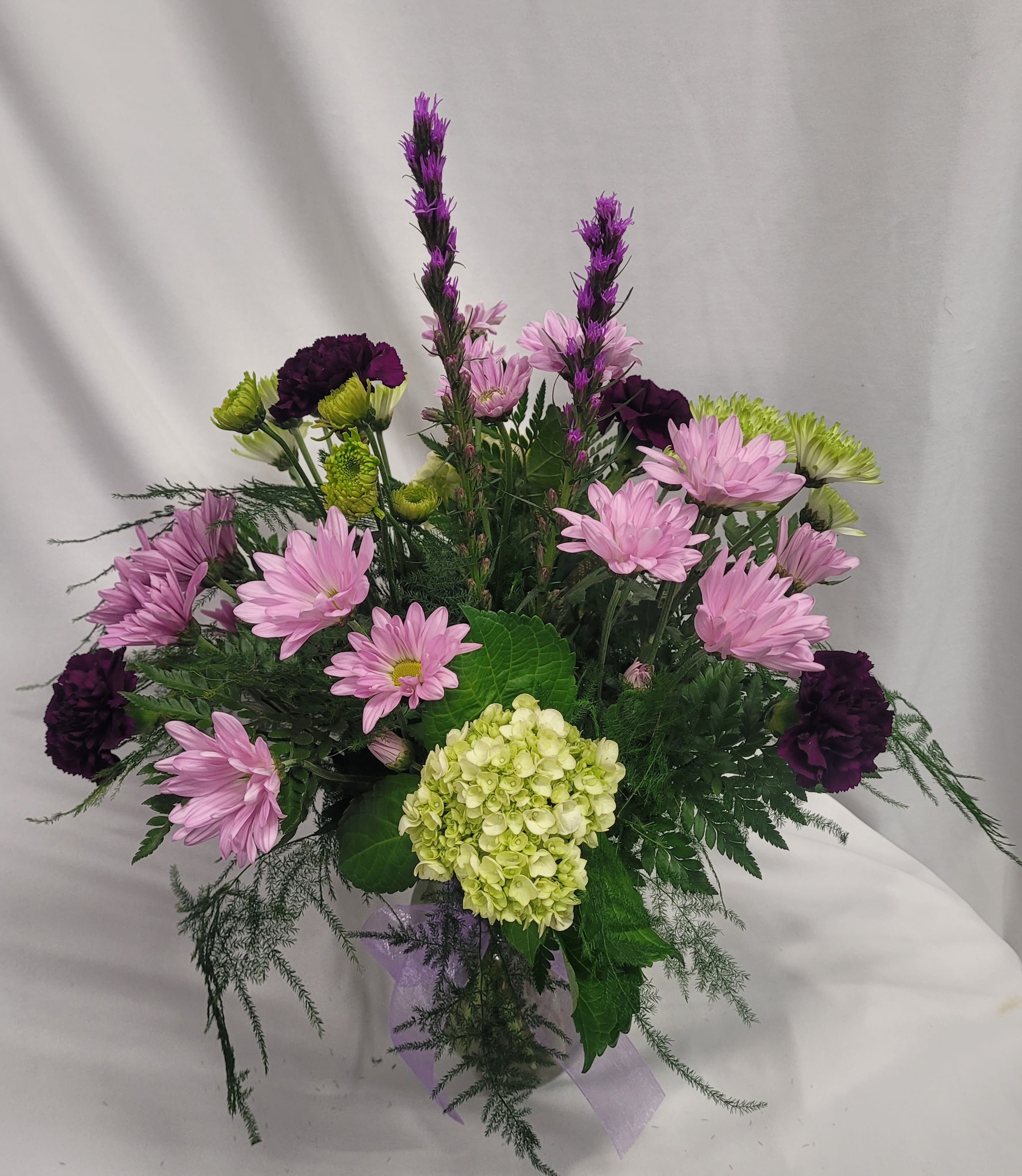 Pink daisies and purple carnations in a clear vase with a hydrangea bloom