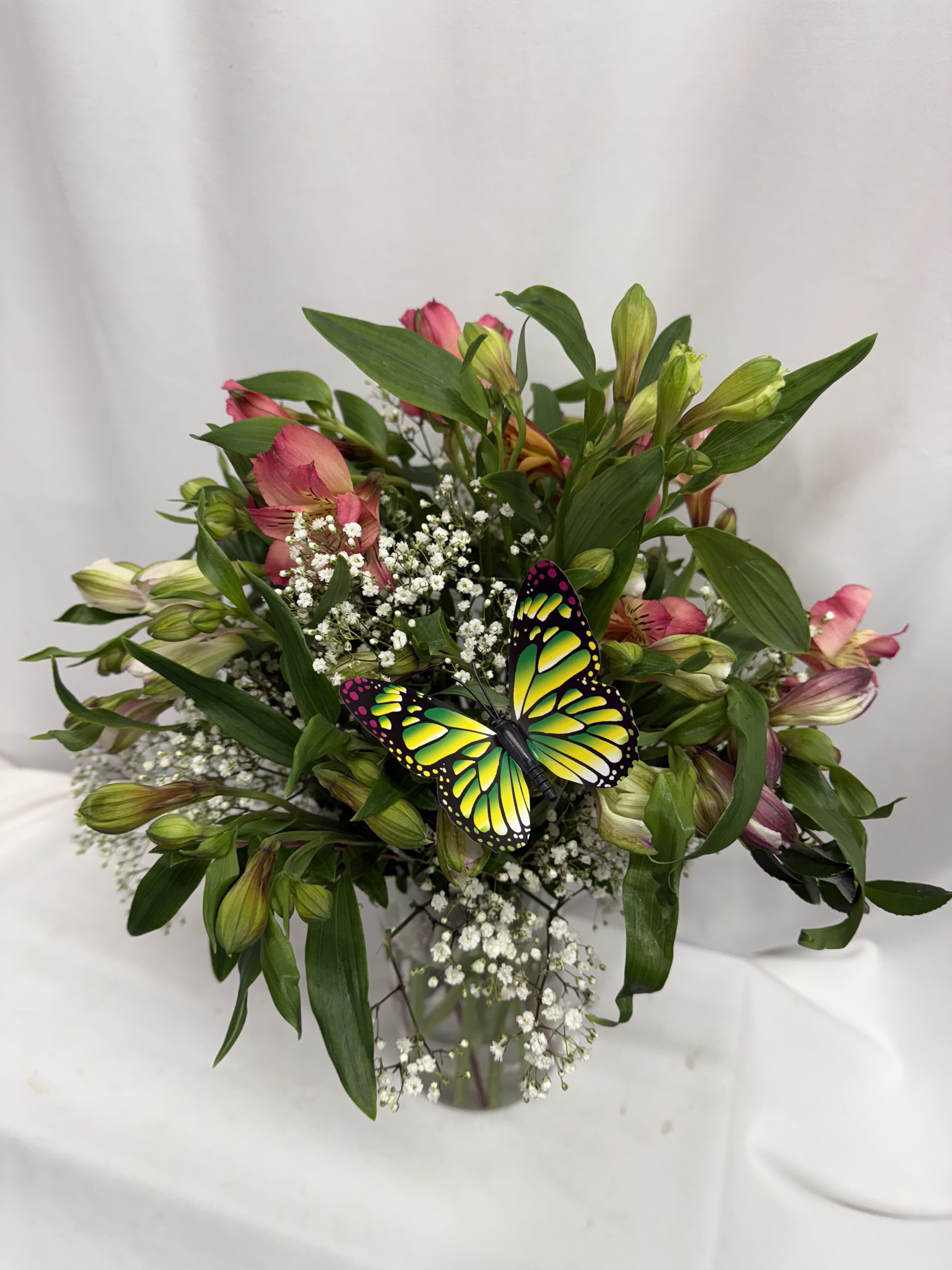 Bouquet of pink alstroemeria with baby's breath and a butterfly pick in a glass vase