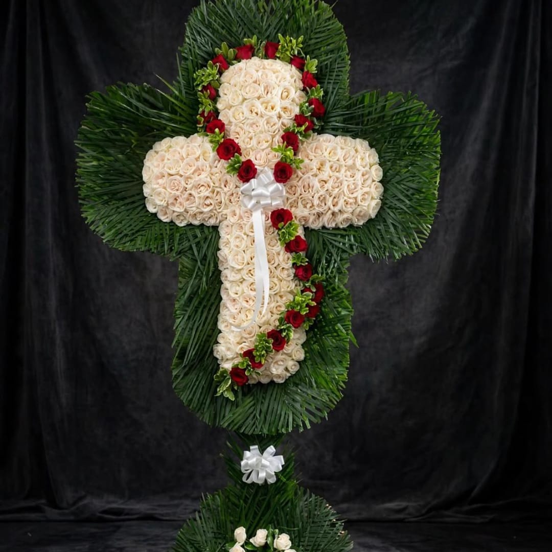 Cross-shaped floral tribute with cream roses, red roses, and white bows