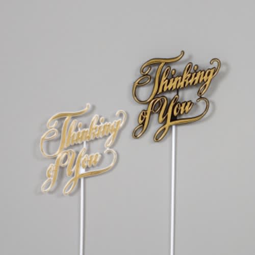 Two gold script cake toppers reading "Thinking of You"