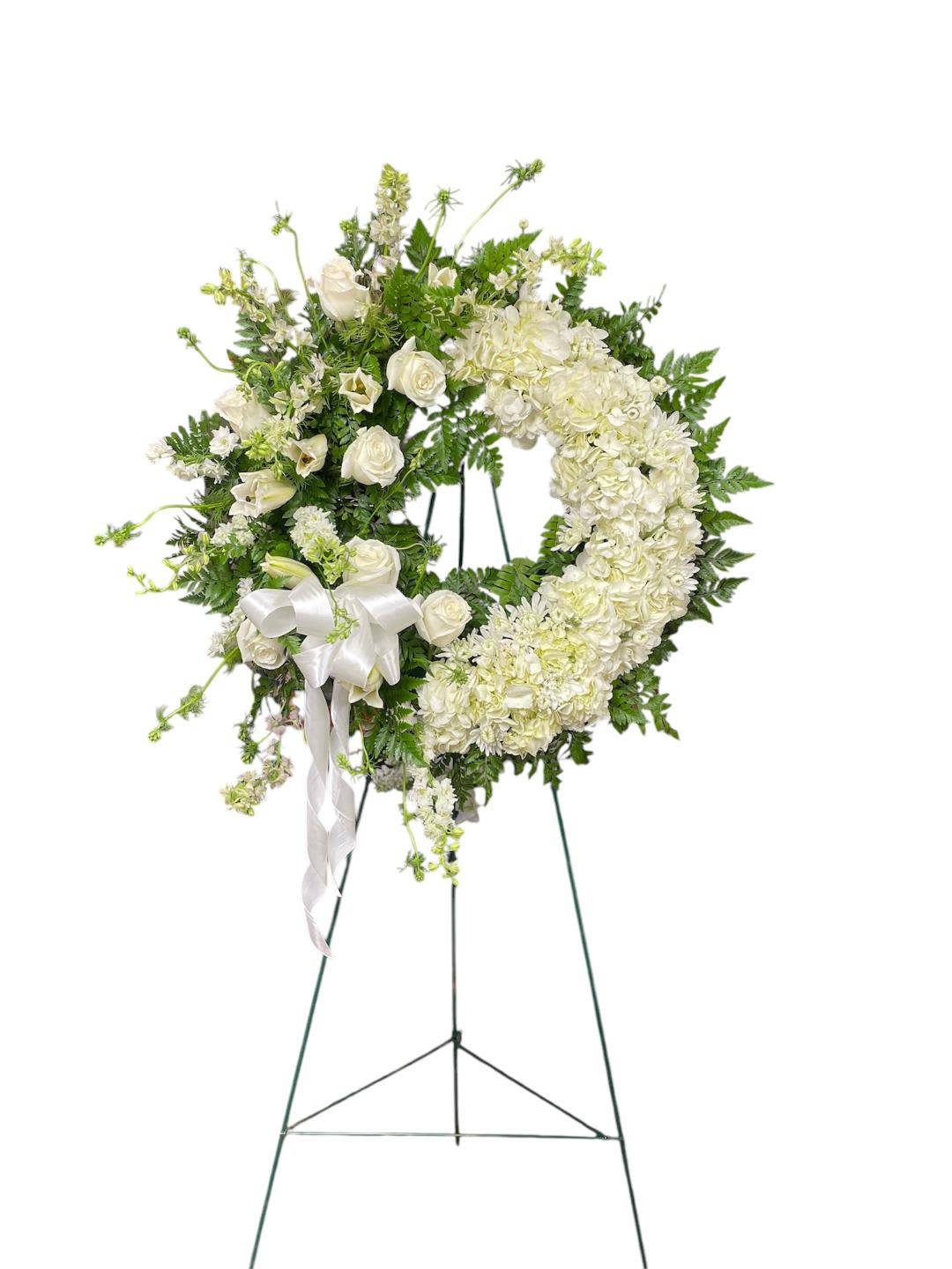 White floral wreath on a standing easel with a ribbon bow
