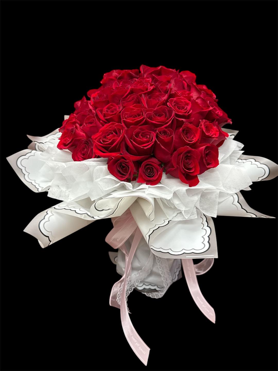 Bouquet of red roses wrapped in white paper with pink ribbons