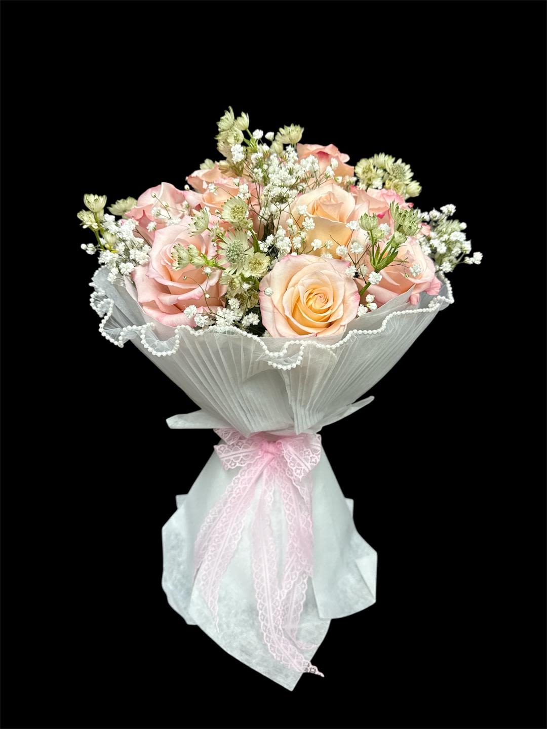 Bouquet of pale pink and peach roses wrapped in white paper with a pink ribbon