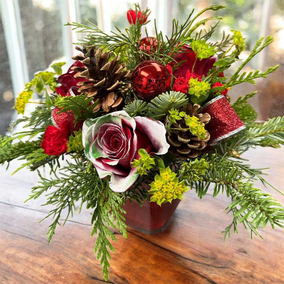 Holiday bouquet with red roses, pinecones, and a red ornament in a vase