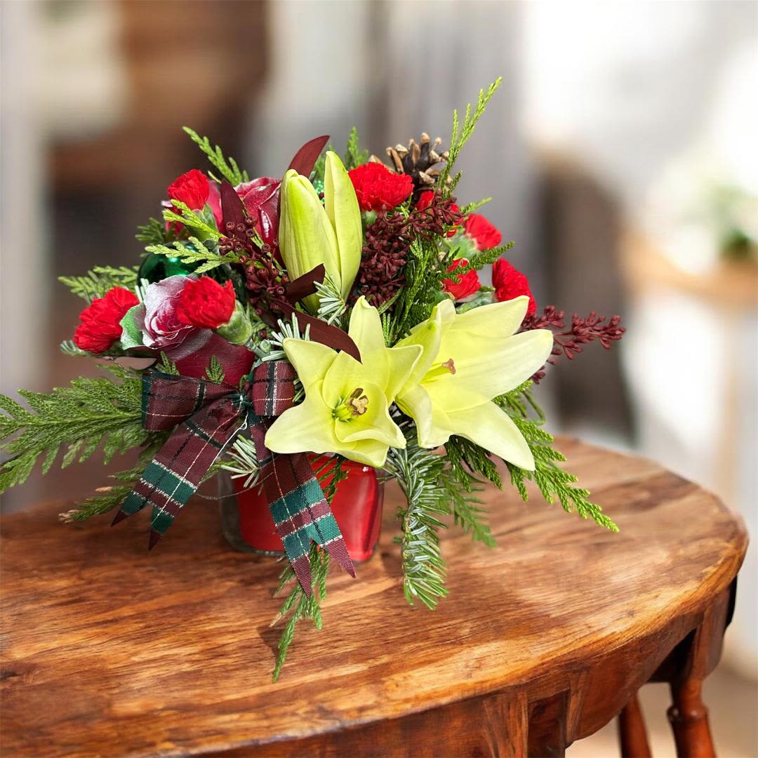 Red and yellow floral arrangement in a red container with plaid ribbon