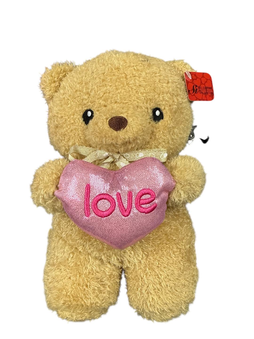 Plush teddy bear holding a pink heart with the word love