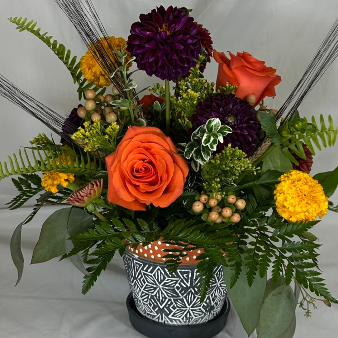 Orange roses and purple dahlias in a patterned pot with fern accents