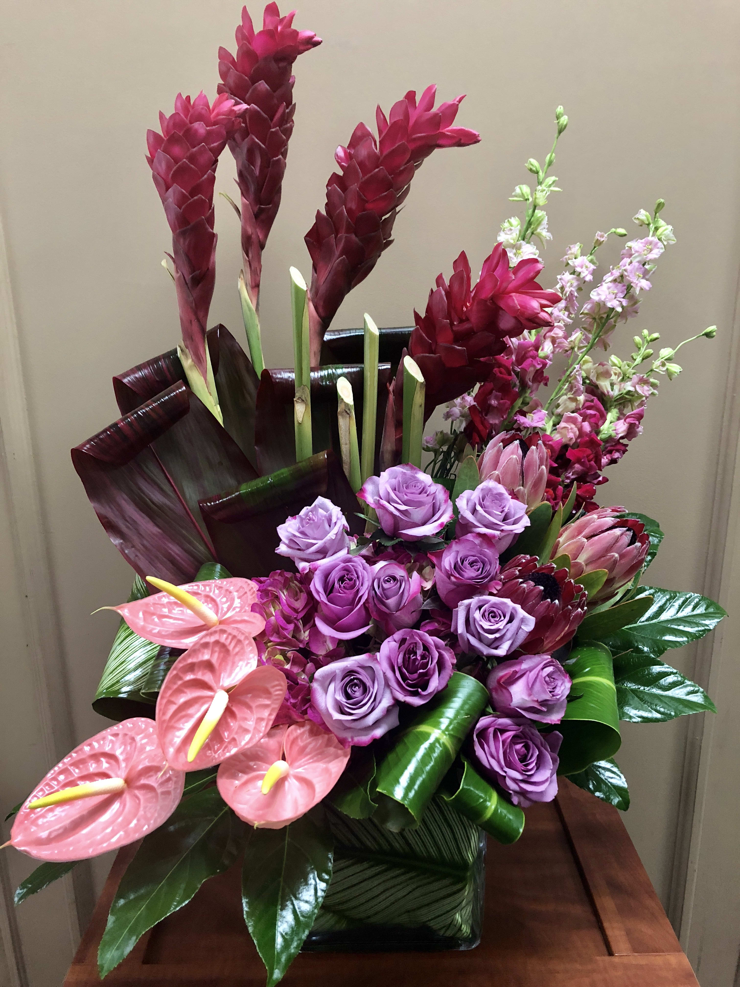 Pink and purple tropical floral arrangement in a square vase