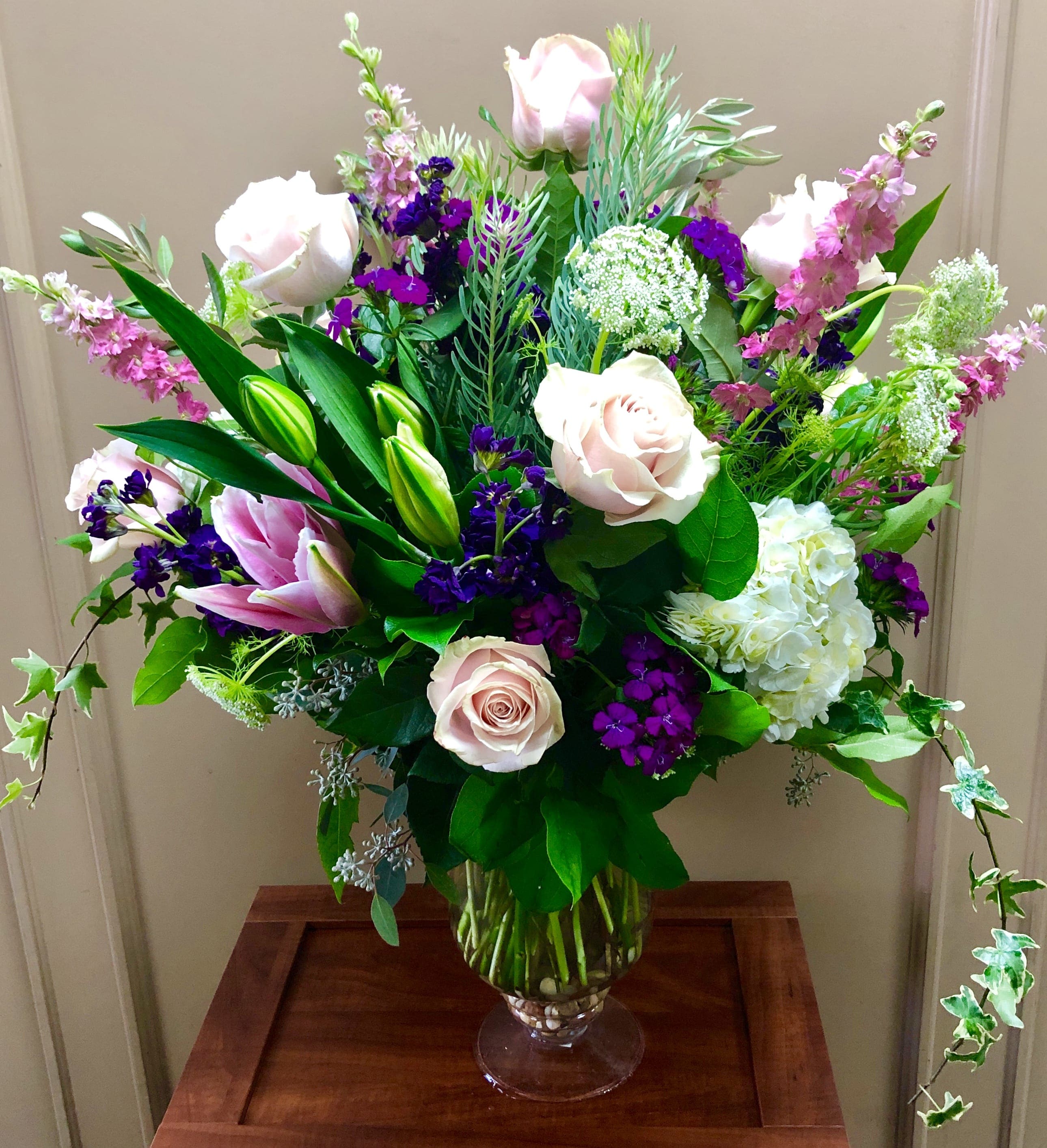 Large bouquet of pink roses, lilies, and purple flowers in a glass vase