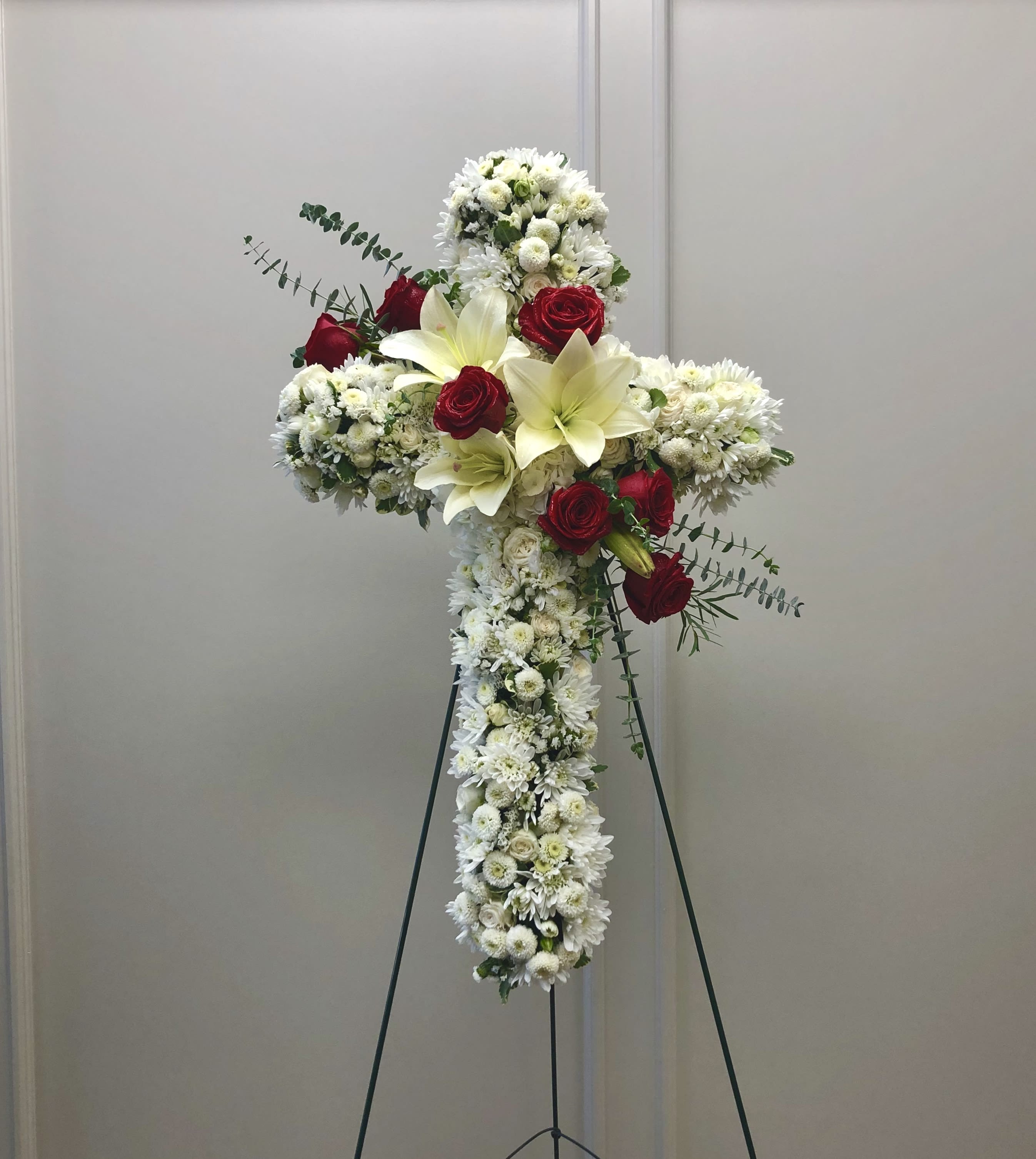 White floral cross arrangement with red roses on a stand