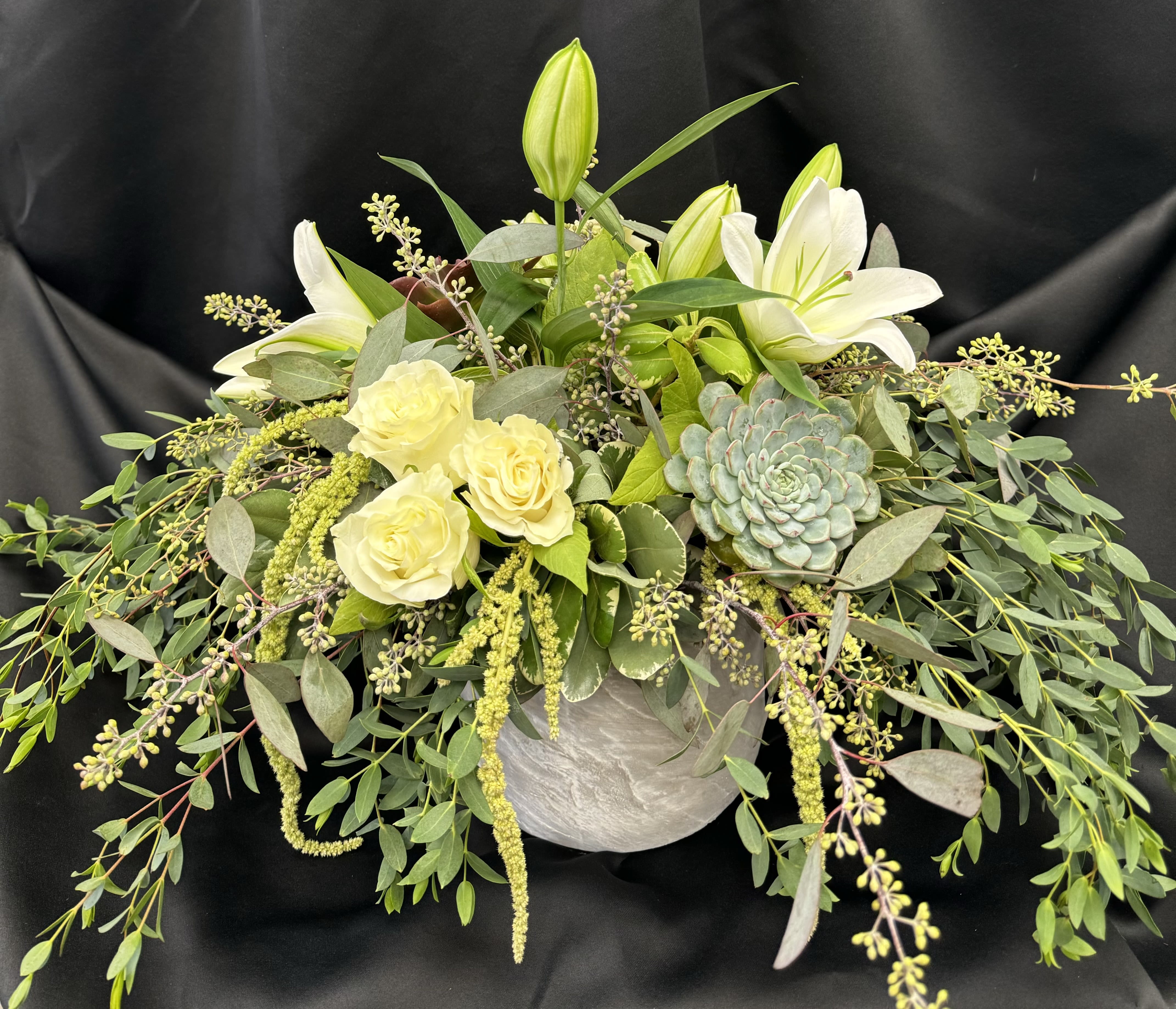 White lilies and pale roses in a low arrangement with a succulent