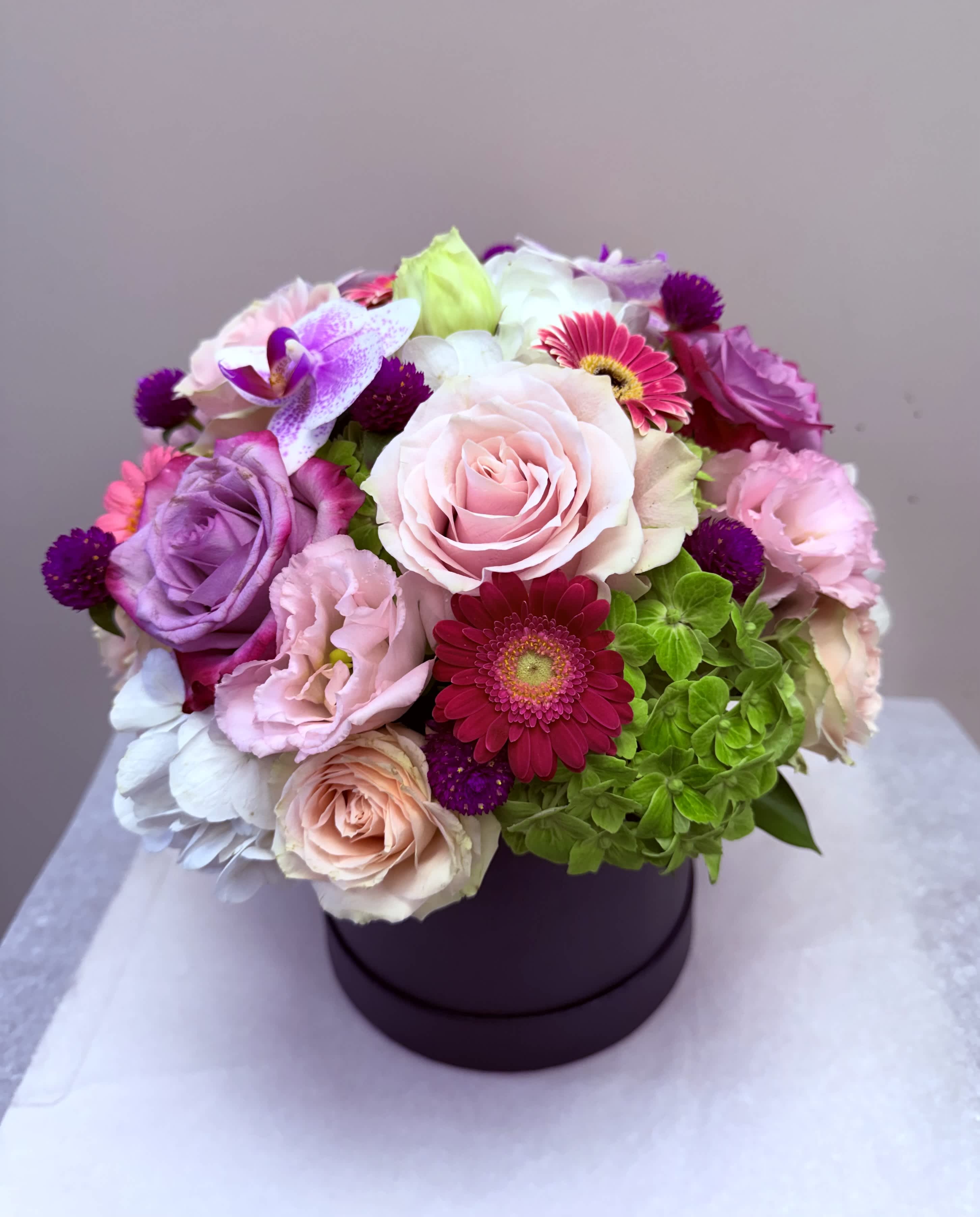 Mixed pink, purple, and white flowers arranged in a round box