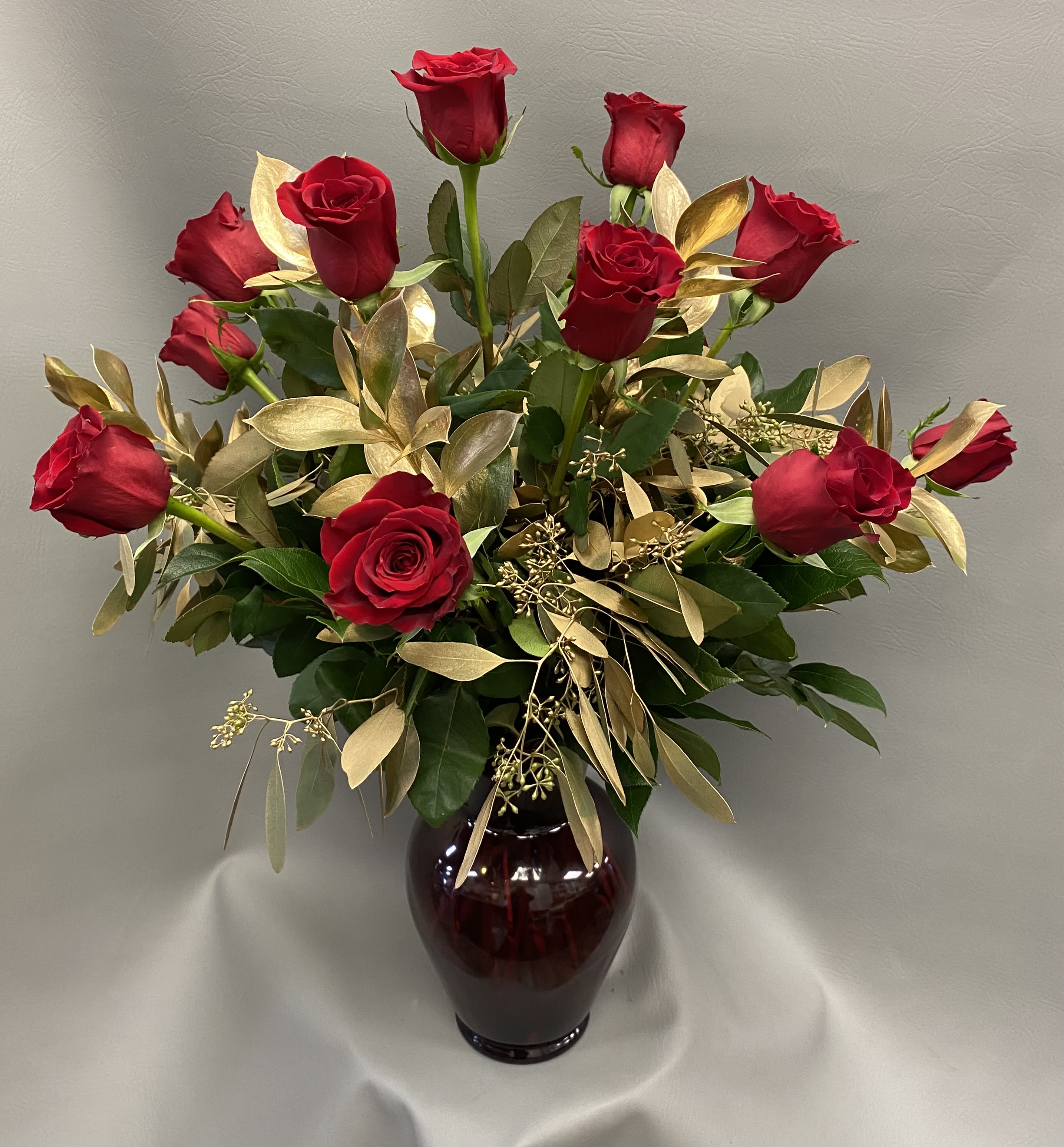 Arrangement of red roses with gold foliage in a dark red glass vase