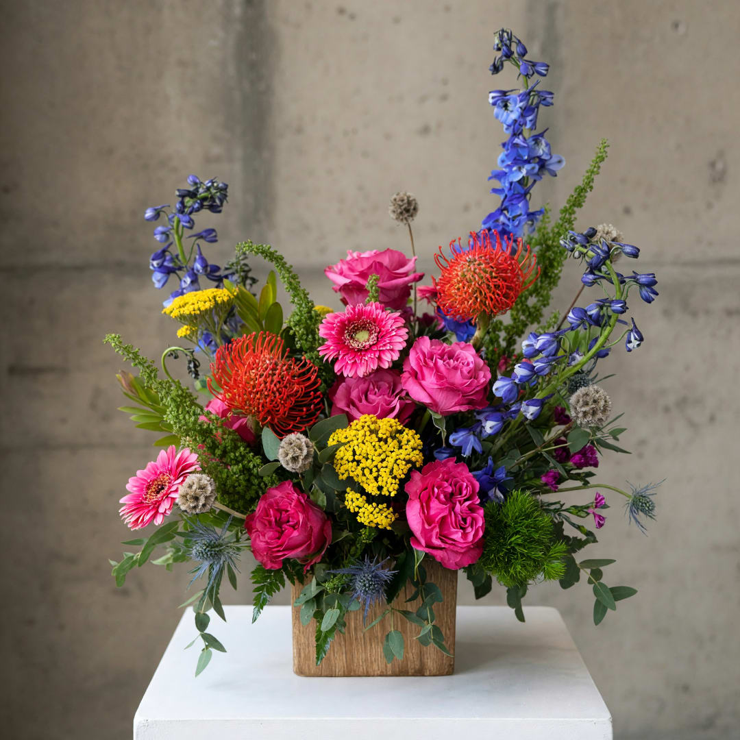 Bright mixed flower arrangement in a wooden box with pink, blue, yellow, and red blooms