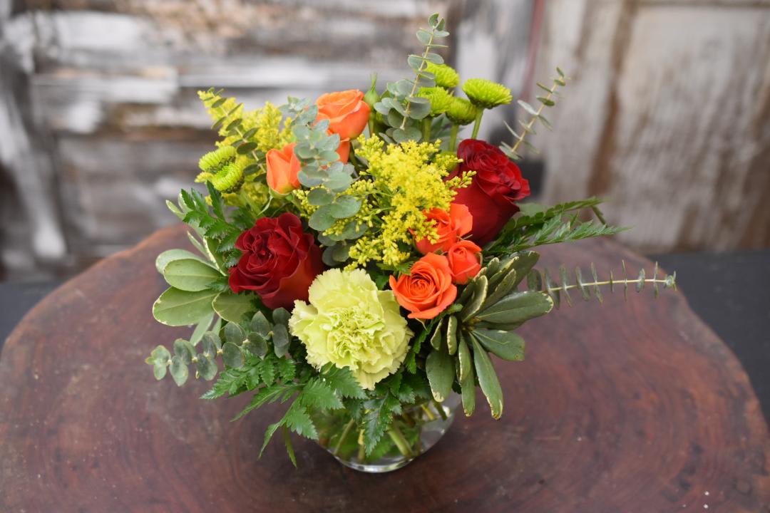 Bouquet of red and orange roses with yellow flowers in a glass vase