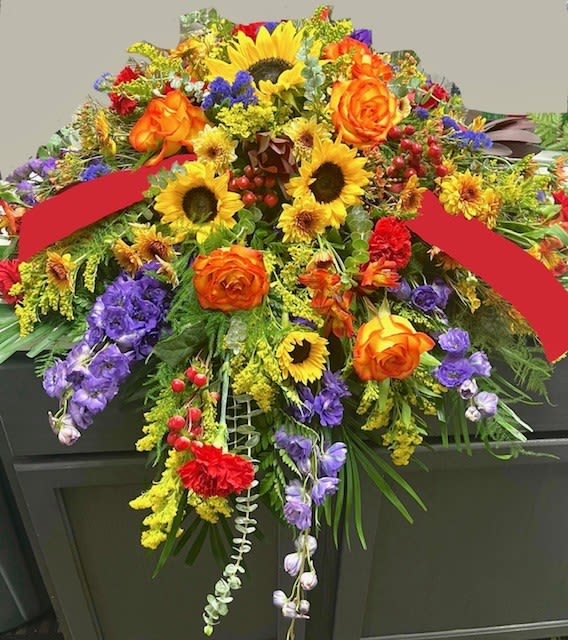 Colorful floral casket spray with sunflowers, orange roses, and purple blooms
