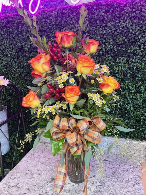 Tall bouquet of orange-yellow roses in a glass vase with a plaid ribbon