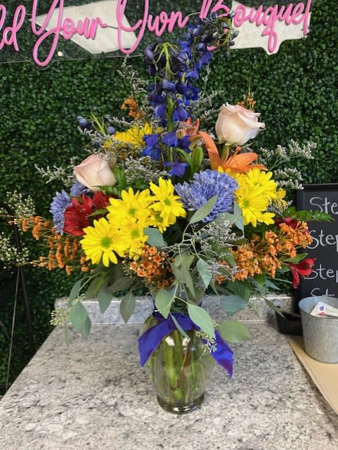 Colorful mixed flower arrangement in a glass vase with a purple ribbon