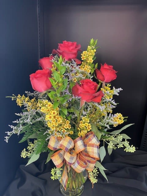 Red roses in a glass vase with yellow filler flowers and a plaid bow