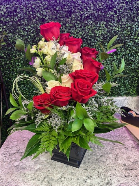 Red and white roses arranged in a black vase with greenery
