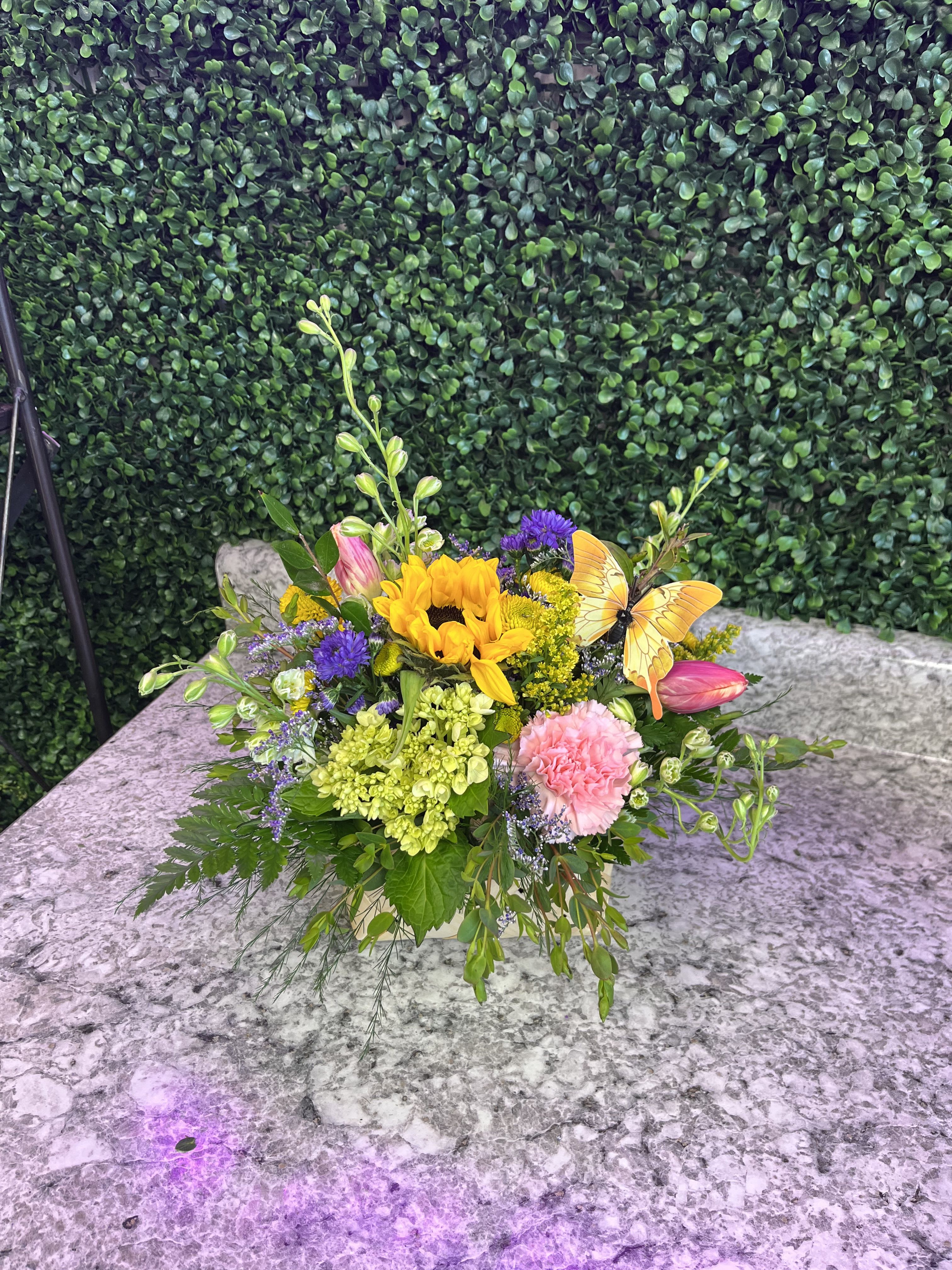 Colorful flower arrangement with a sunflower, pink blooms, and a butterfly pick in a low container