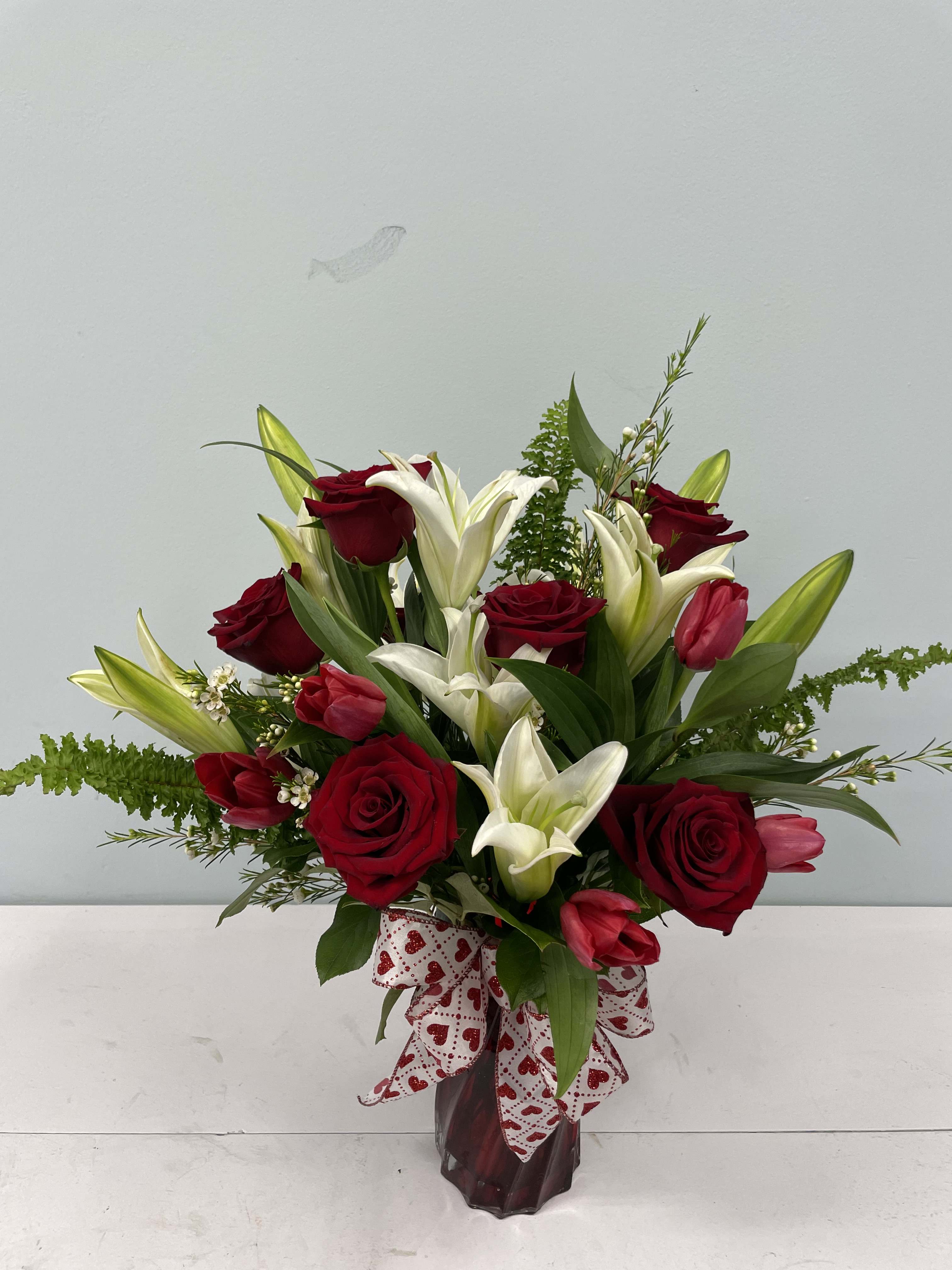Red roses and white lilies in a glass vase with a heart-patterned ribbon