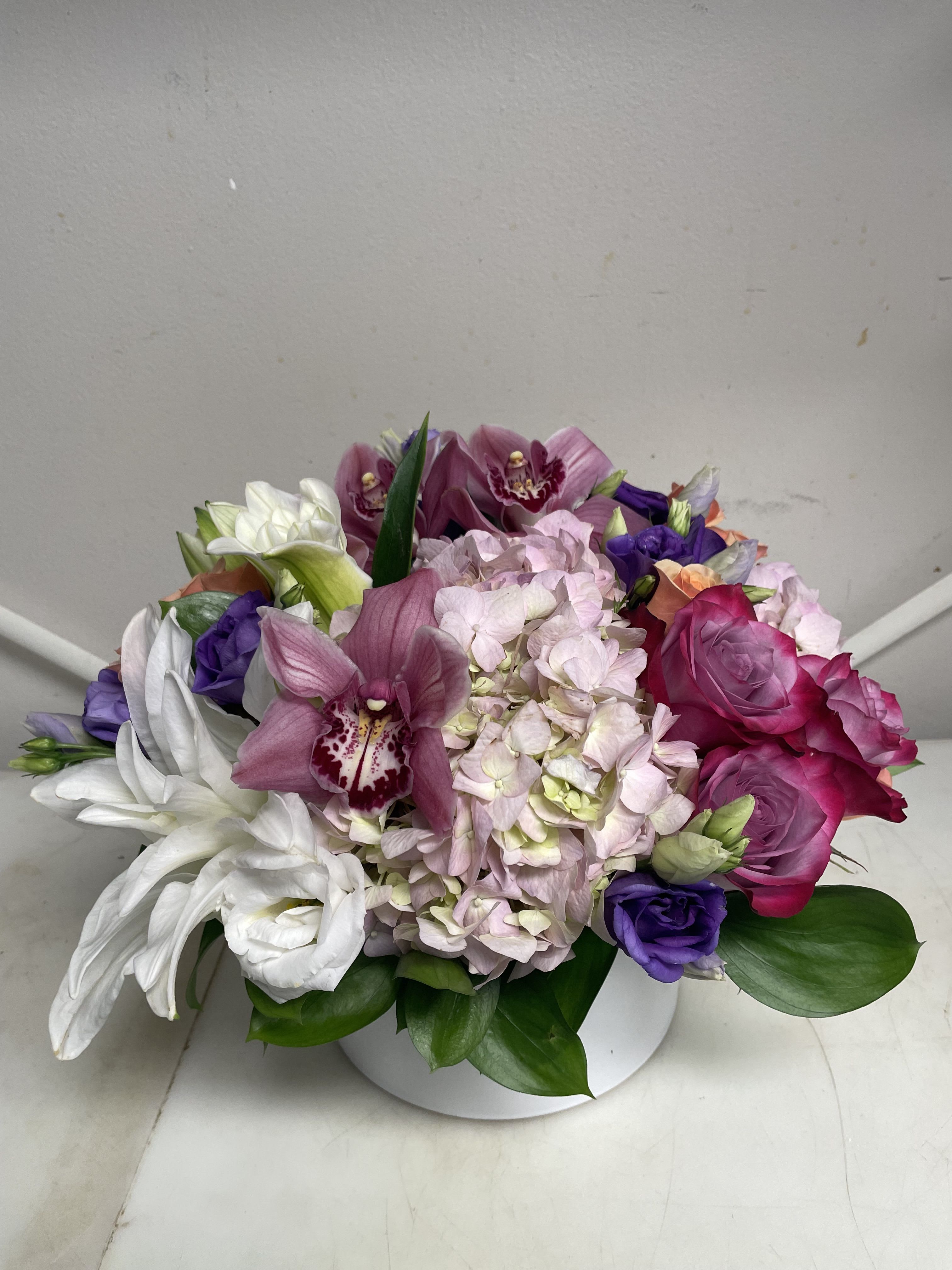 Mixed bouquet with pink roses, hydrangea, orchids, and white lilies in a white vase