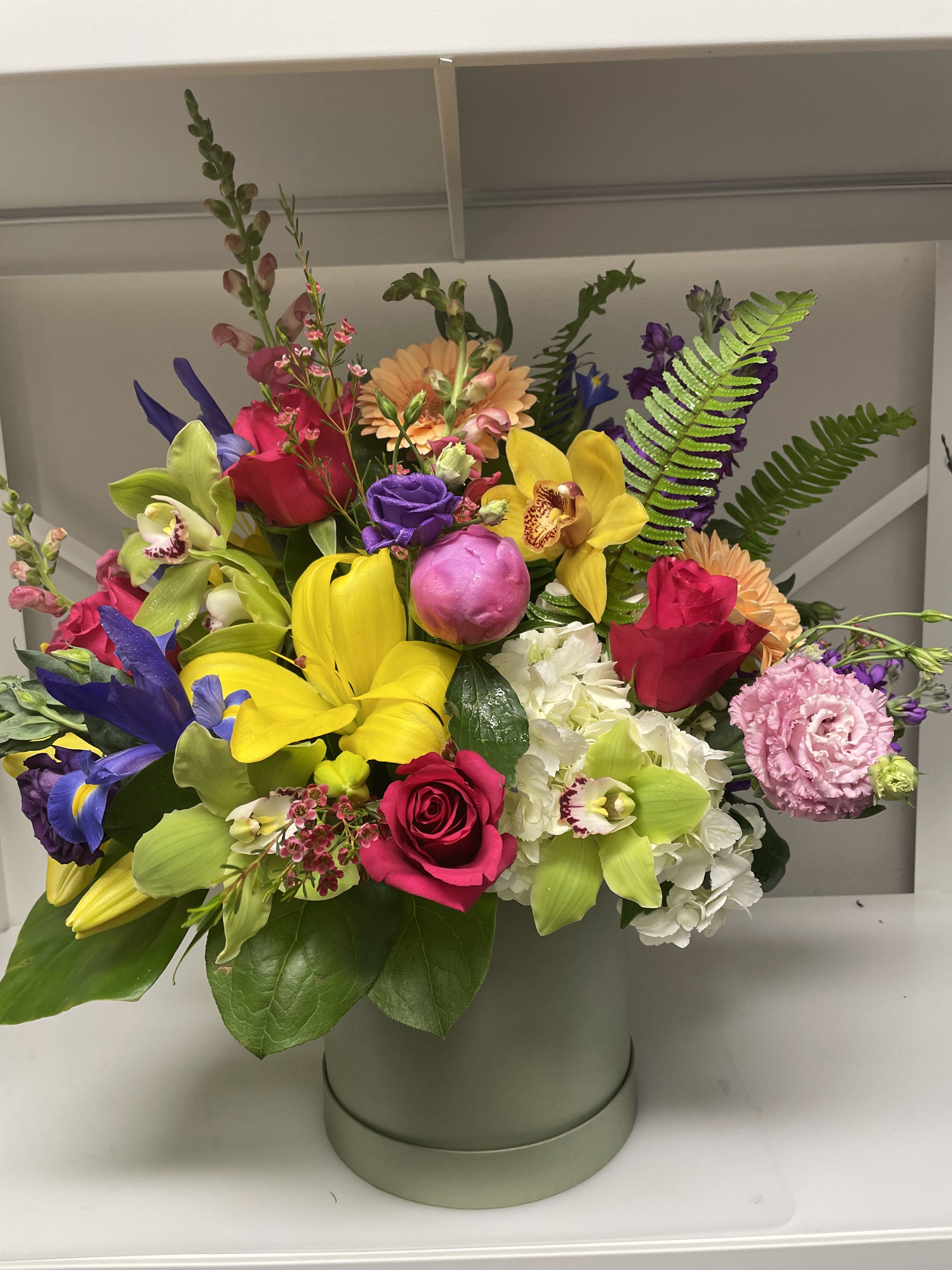 Bright mixed bouquet in a round hatbox with roses, orchids, lilies, and hydrangea