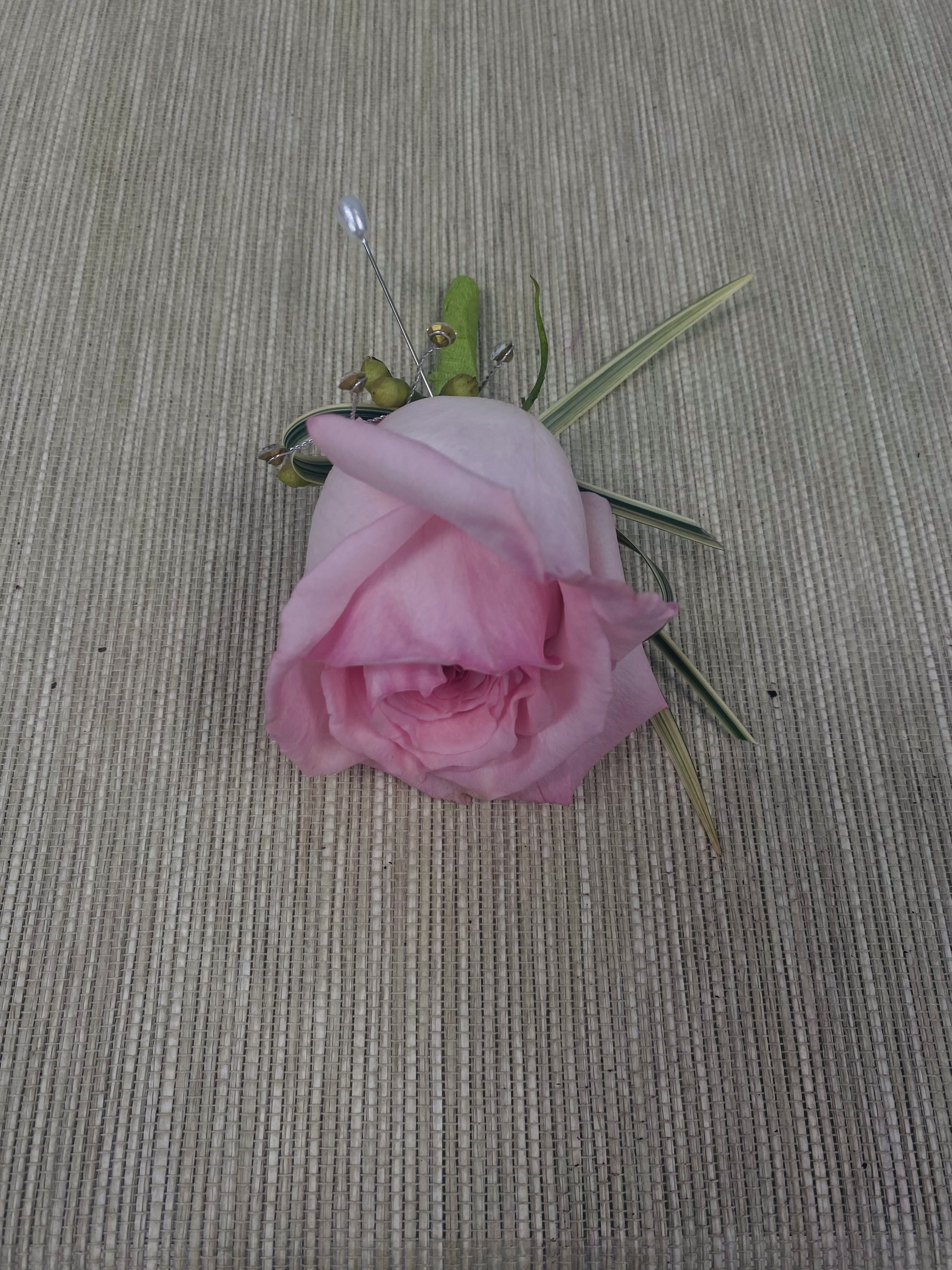Pink rose boutonniere with decorative grass accents on a woven surface